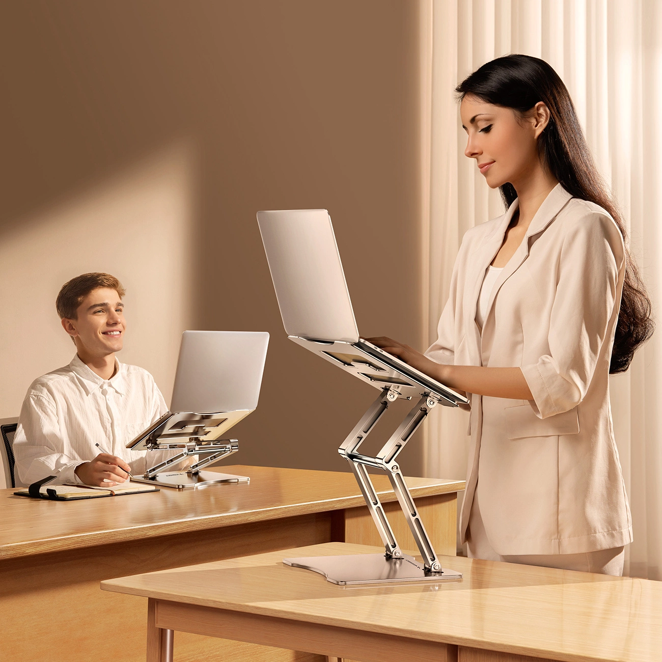 Zwei Personen arbeiten mit Laptops auf Ständern. Eine Frau steht, ein Mann sitzt. Beide befinden sich in einem hellen Büroumfeld.