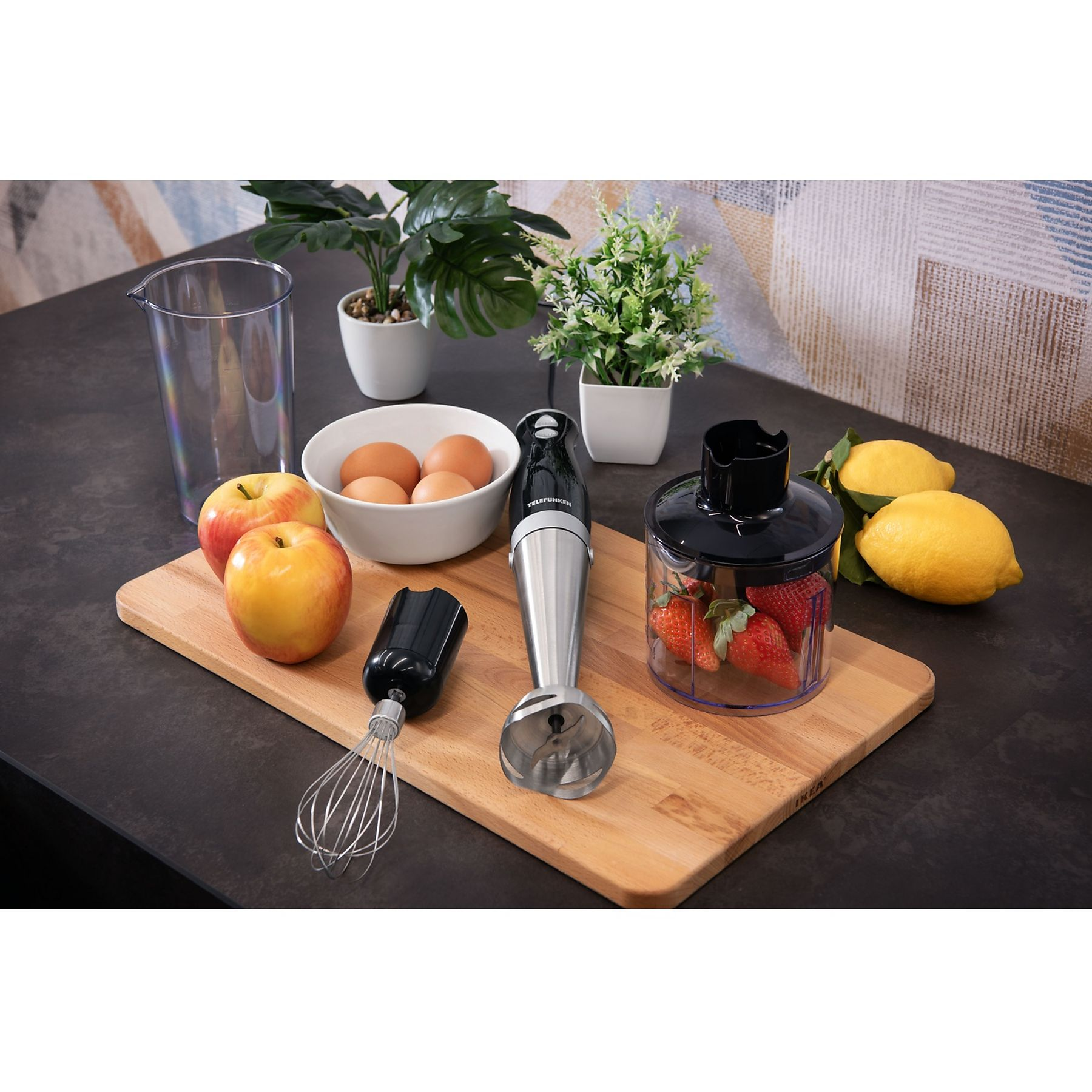 Una scena di cucina con frullatore, frutta, uova, piante e tagliere. Il frullatore è al centro.