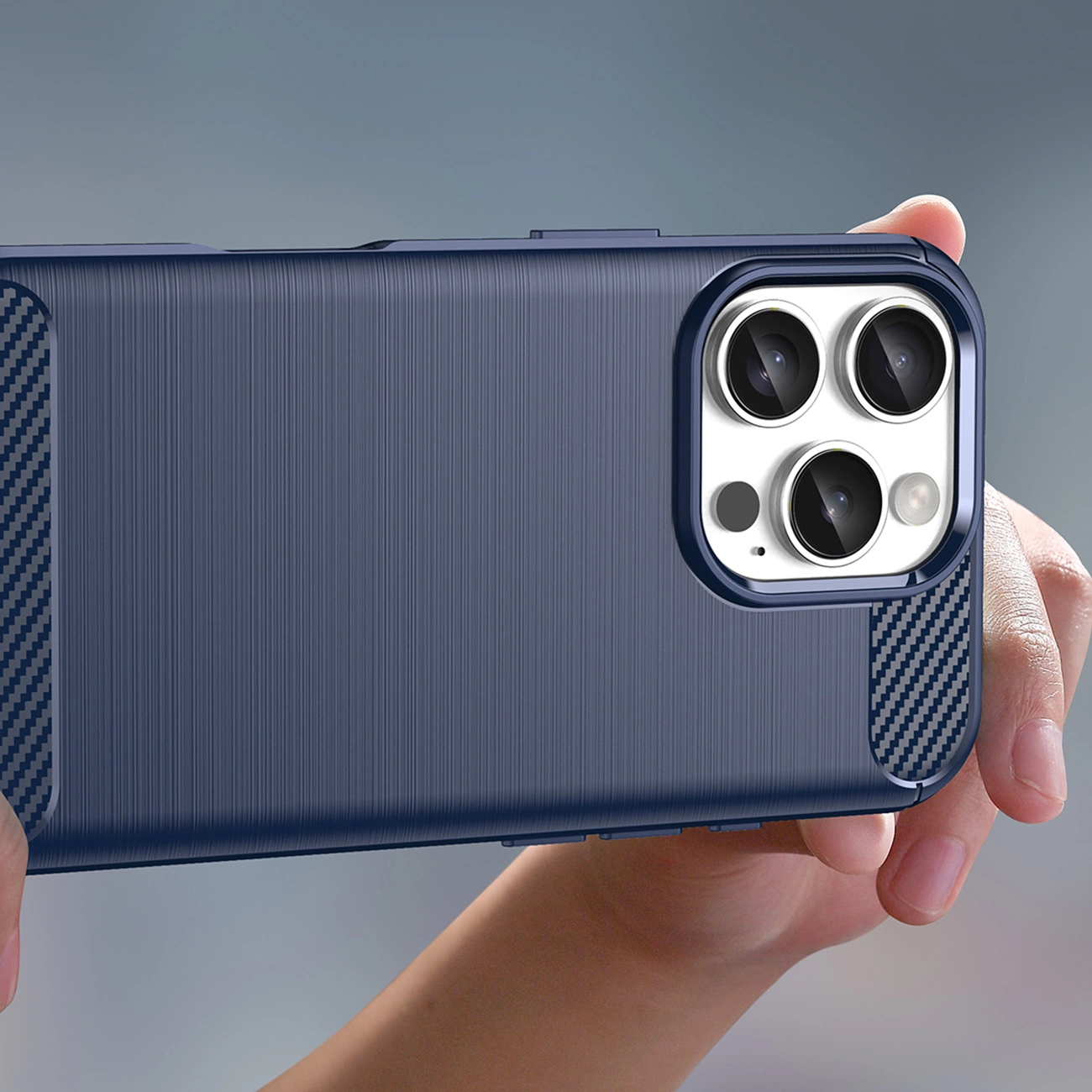 Una mano tiene una custodia per telefono blu scuro. La custodia ha un retro strutturato e un ritaglio per la fotocamera con tre lenti. Accenti in fibra di carbonio sono visibili.