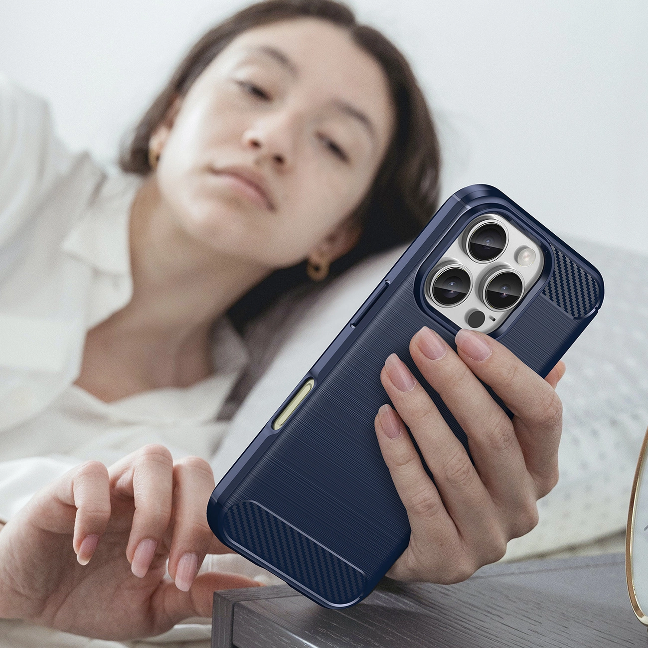 Una donna a letto tiene in mano una custodia per telefono blu scuro. La custodia del telefono è il fulcro, con il volto della donna leggermente sfocato.