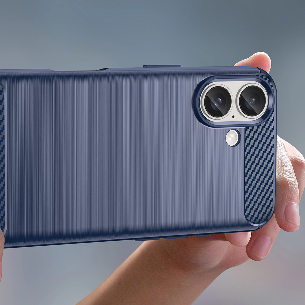 Una persona tiene in mano una custodia blu per telefono con due lenti della fotocamera e un flash. La custodia ha una superficie strutturata e dettagli in fibra di carbonio.