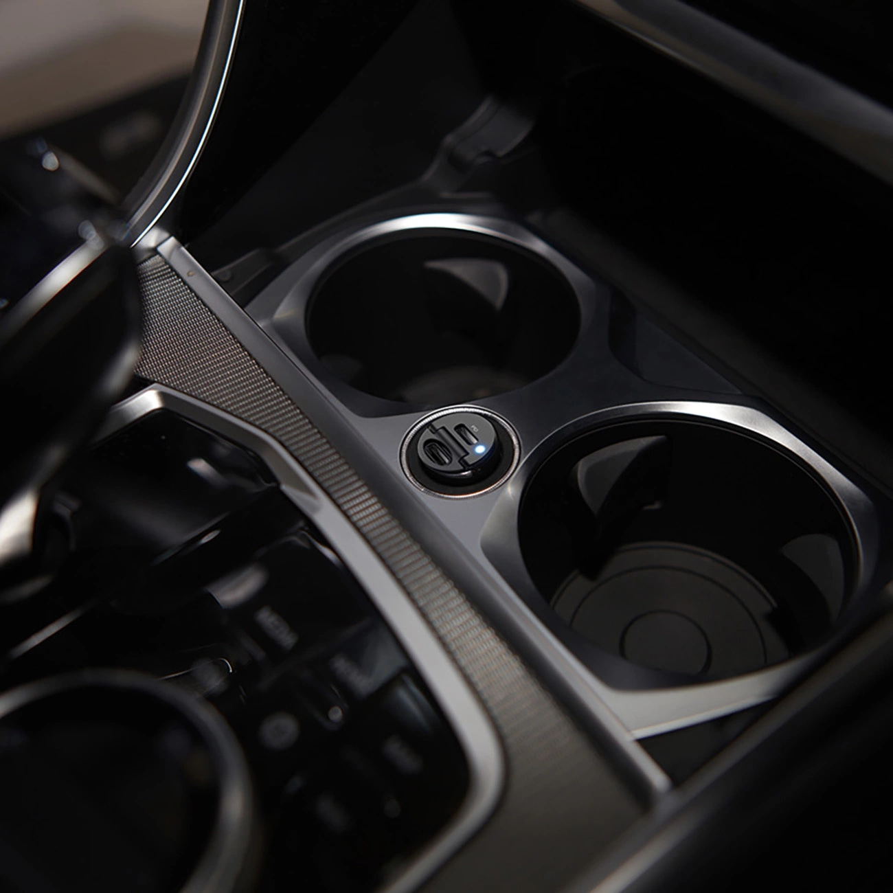 Console centrale dell'auto con due portabicchieri e una porta USB. Interni argento e neri con un design moderno e illuminazione ambientale.