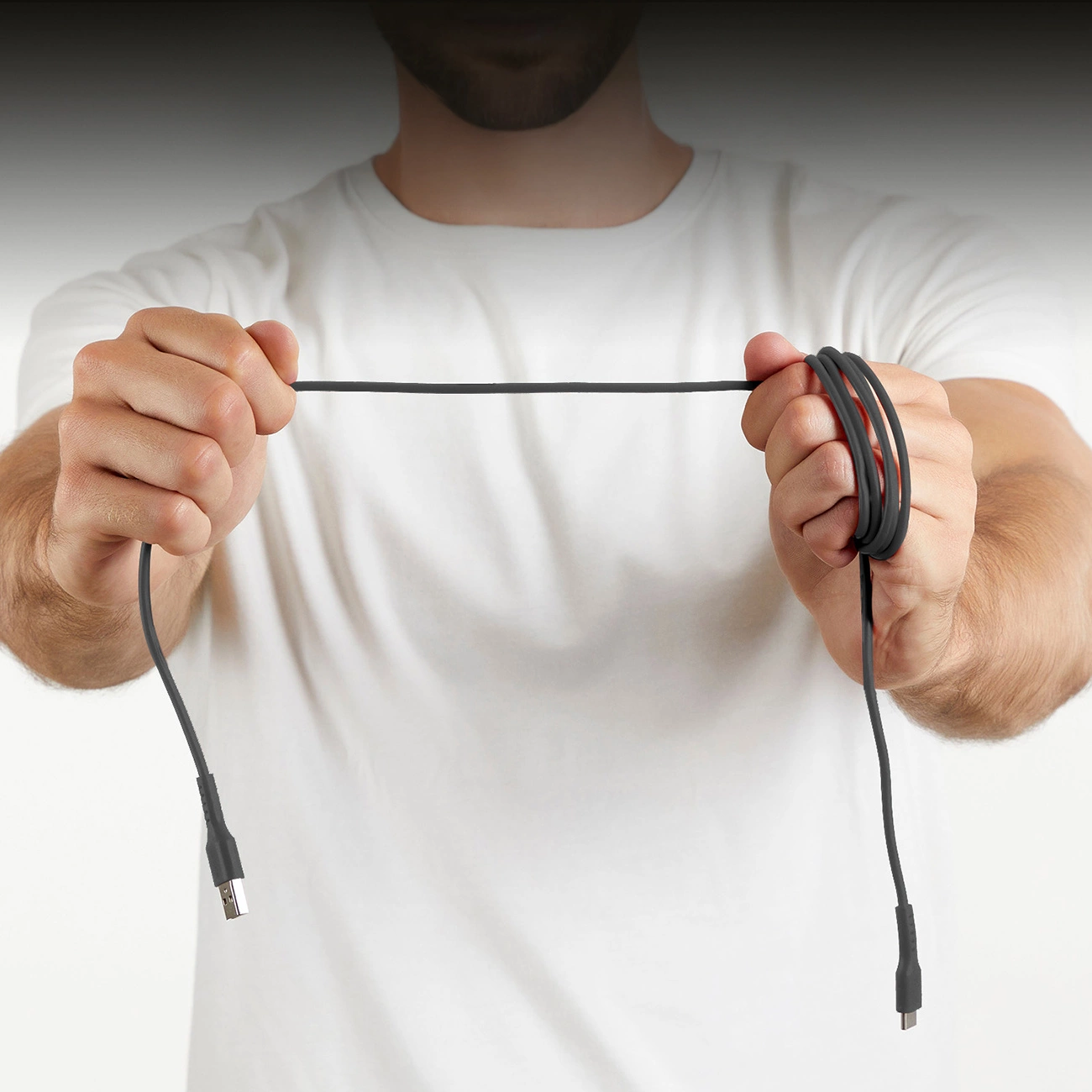 Un uomo tiene un cavo nero davanti a uno sfondo bianco. Il cavo è ad anello in una mano e dritto nell'altra.