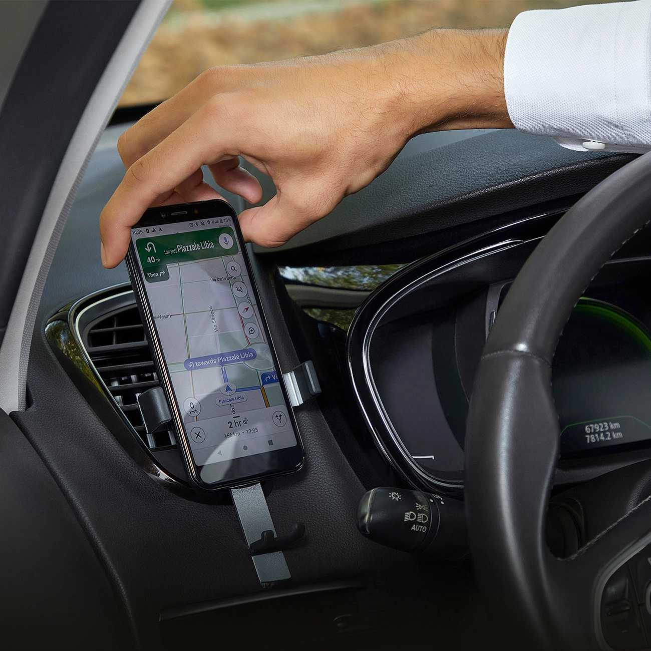 Una mano posiziona uno smartphone con un'app di navigazione in un supporto per auto. L'interno dell'auto è visibile, compreso il volante e il cruscotto.
