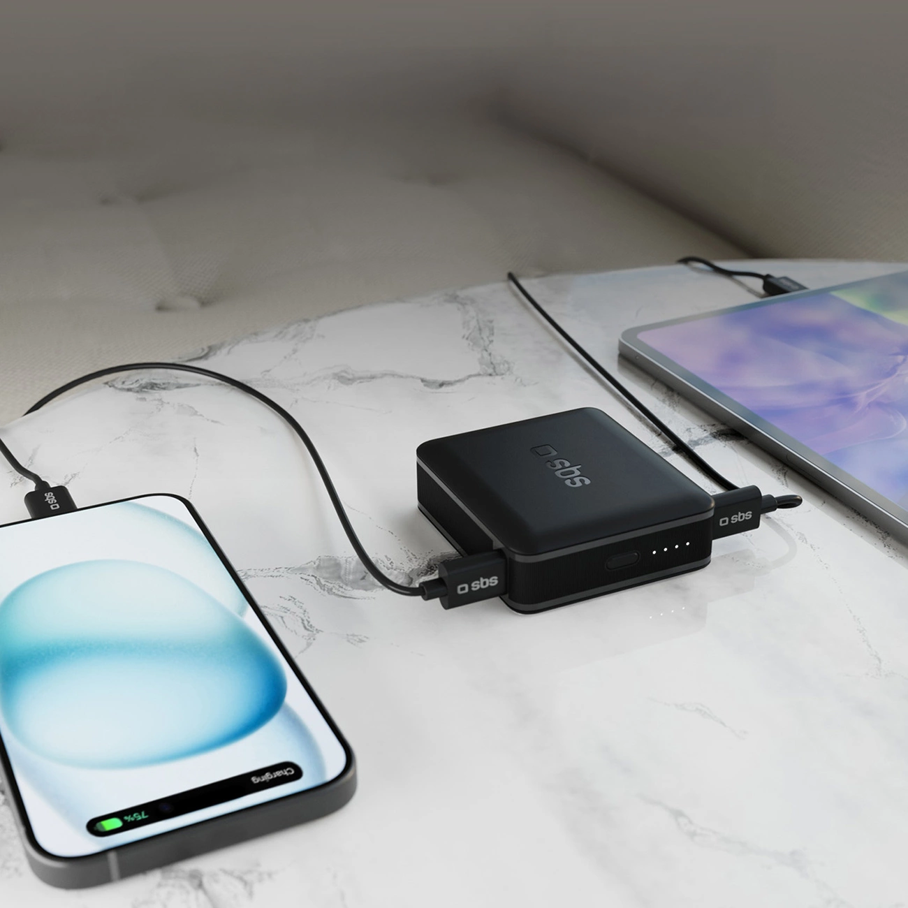 Telefon, tablet i power bank na marmurowym stole. Telefon i tablet ładują się z power banku. Telefon pokazuje 75% naładowania.