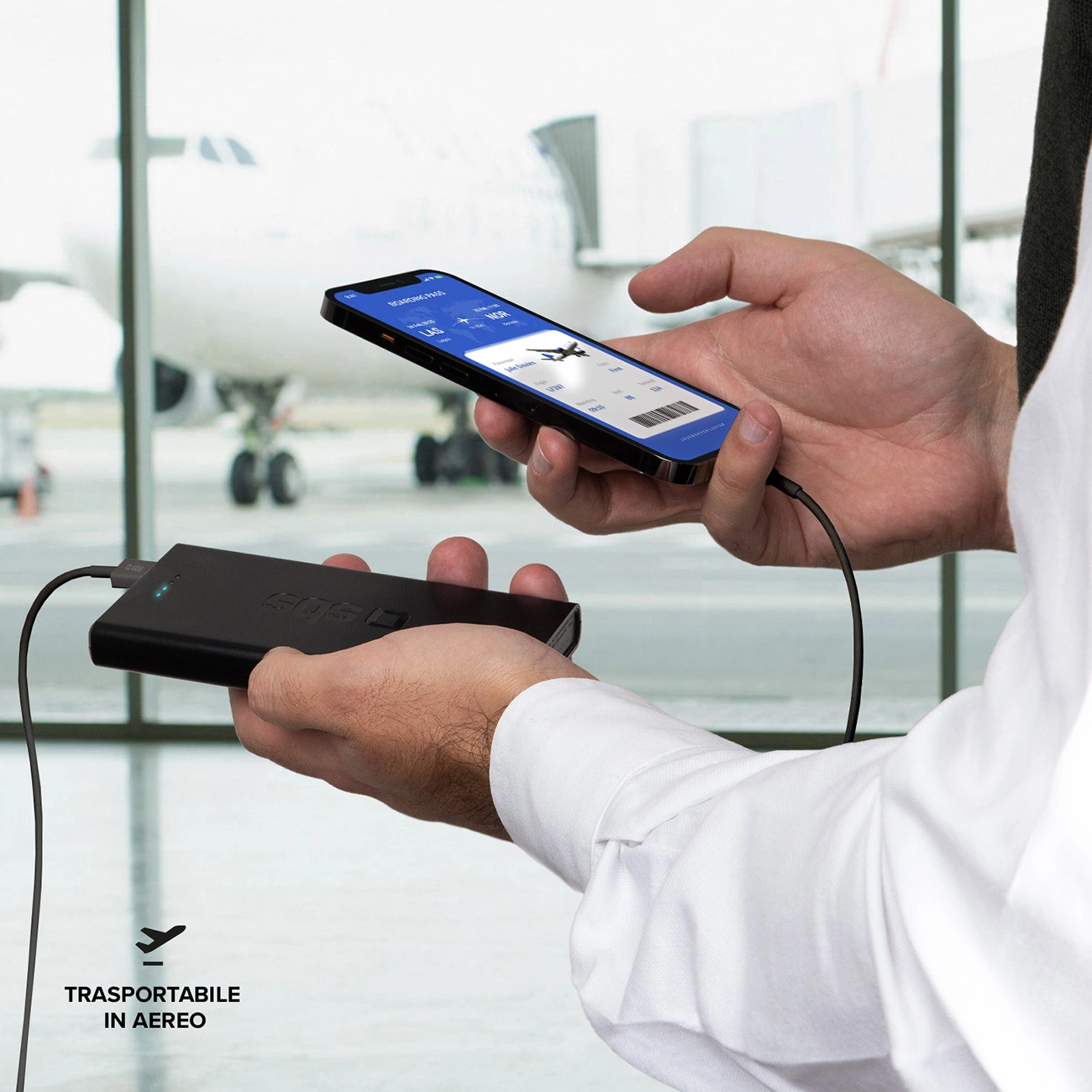 Una persona tiene in mano un telefono con una carta d'imbarco, collegato a un power bank. Aereo sullo sfondo.