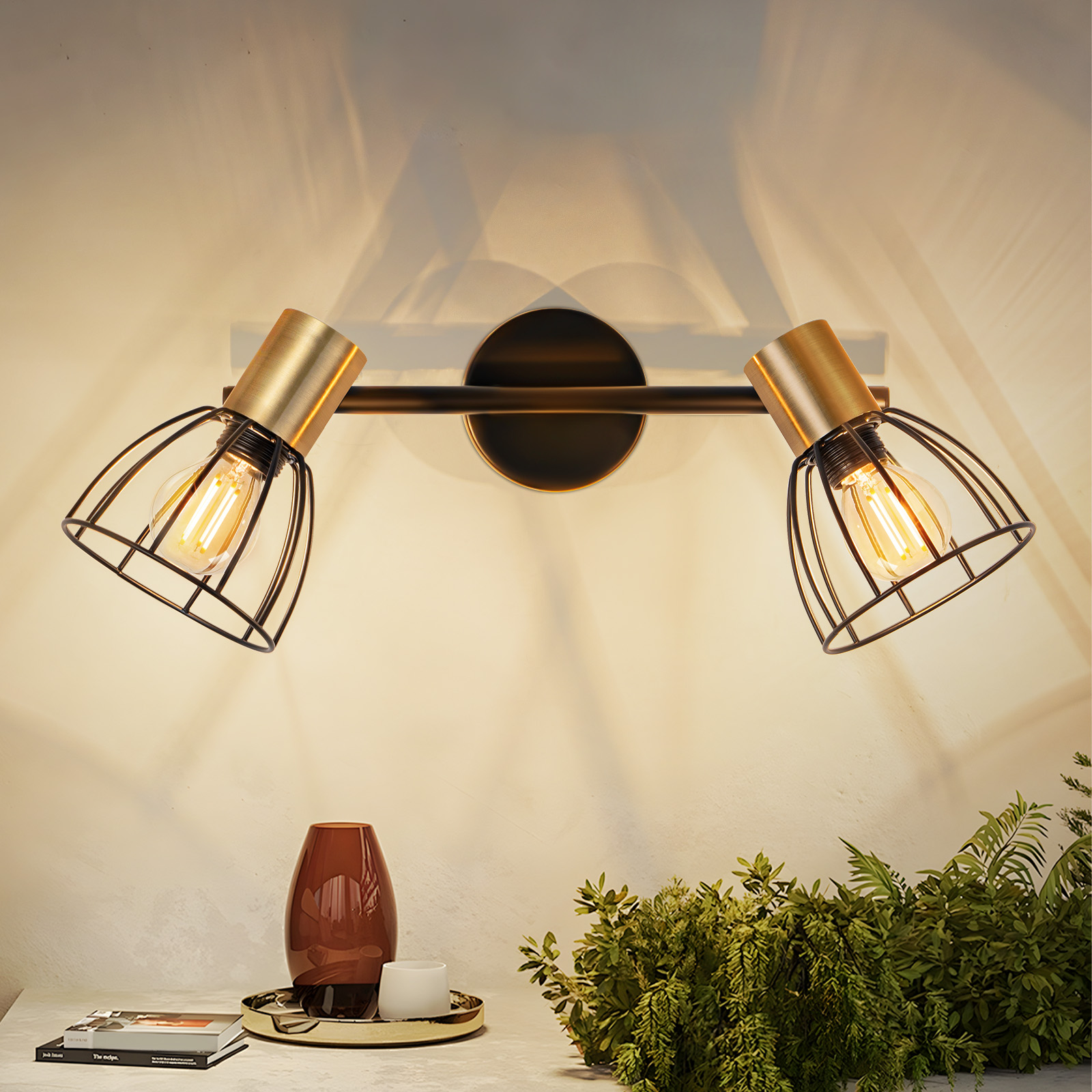 Due lampade oro e nere con paralumi a gabbia. Un vaso marrone e vegetazione sottostante.