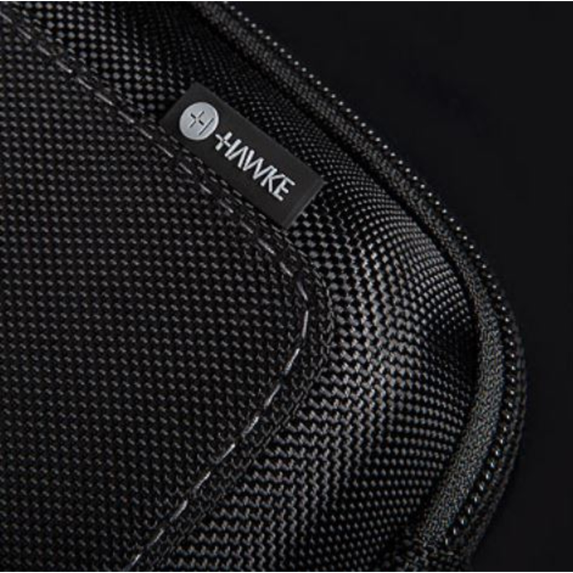 Nahaufnahme einer schwarzen Tasche mit strukturiertem Muster. Ein kleines Etikett mit dem 'Hawke'-Logo ist sichtbar.