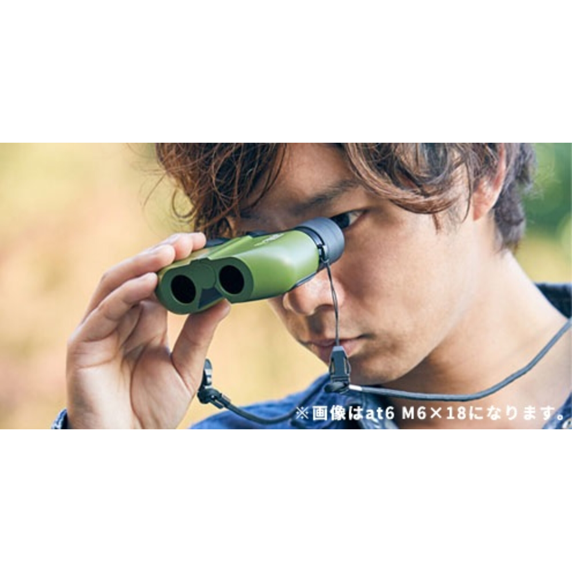 Ein Mann schaut durch ein grünes Fernglas. Der Hintergrund ist verschwommene Natur. Das Fernglas hat einen Nackengurt.