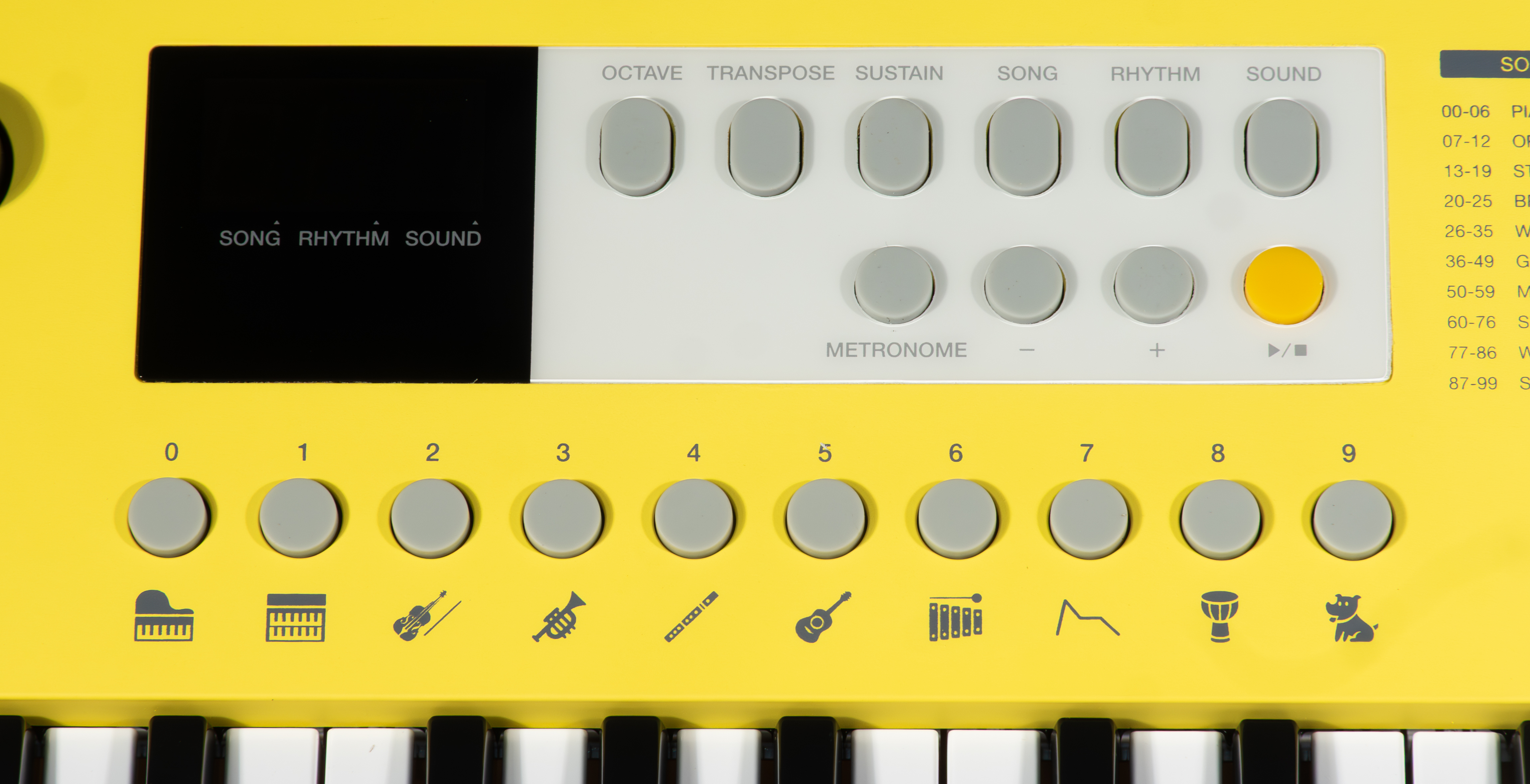 Eine gelbe Tastatur mit grauen Knöpfen. Oben befinden sich Funktionstasten. Unten befinden sich Klaviertasten. Zahlen und Instrumentensymbole sind vorhanden.