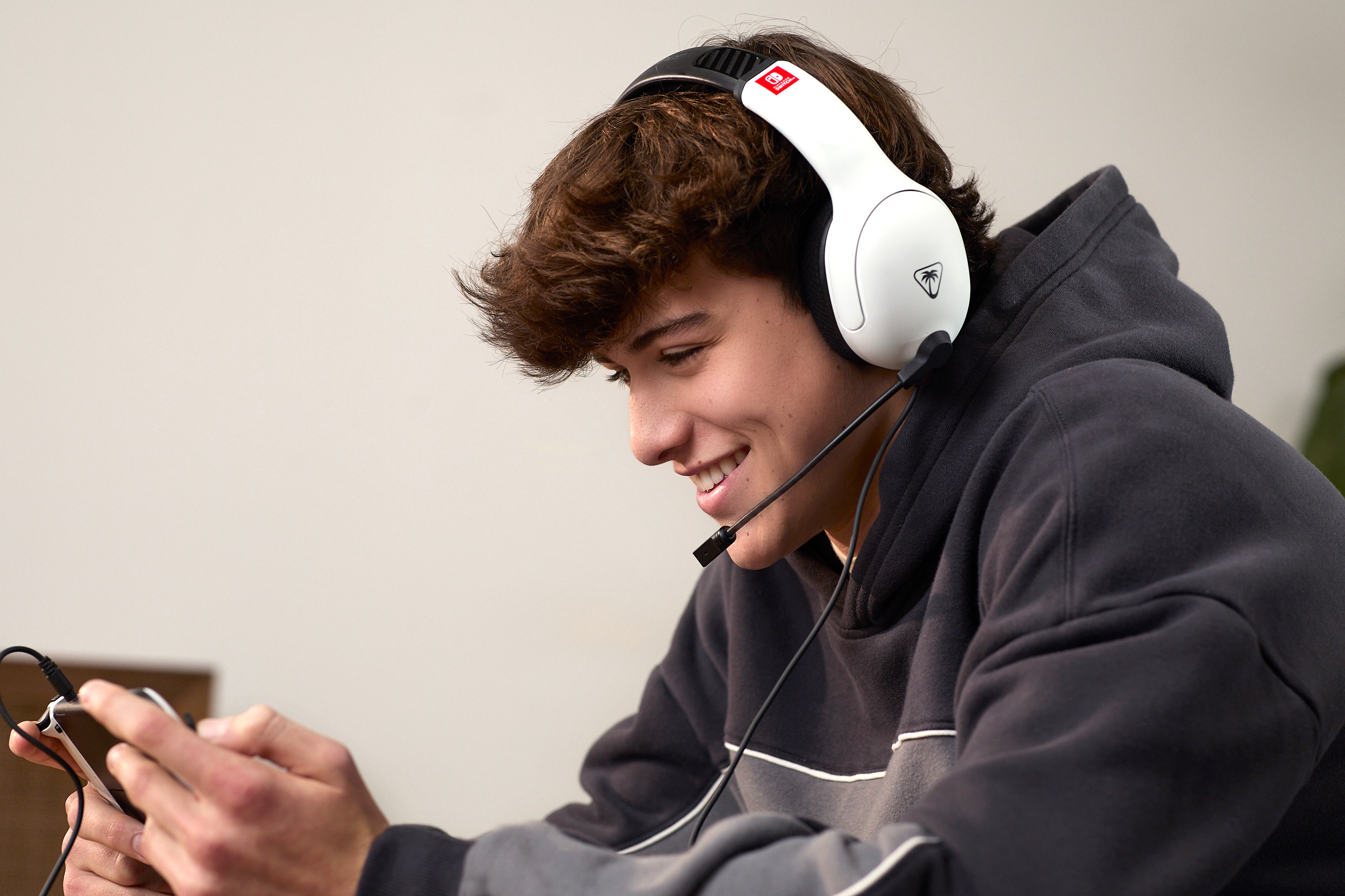 Uśmiechnięty nastolatek z zestawem słuchawkowym i urządzeniem. Tło to gładka ściana.