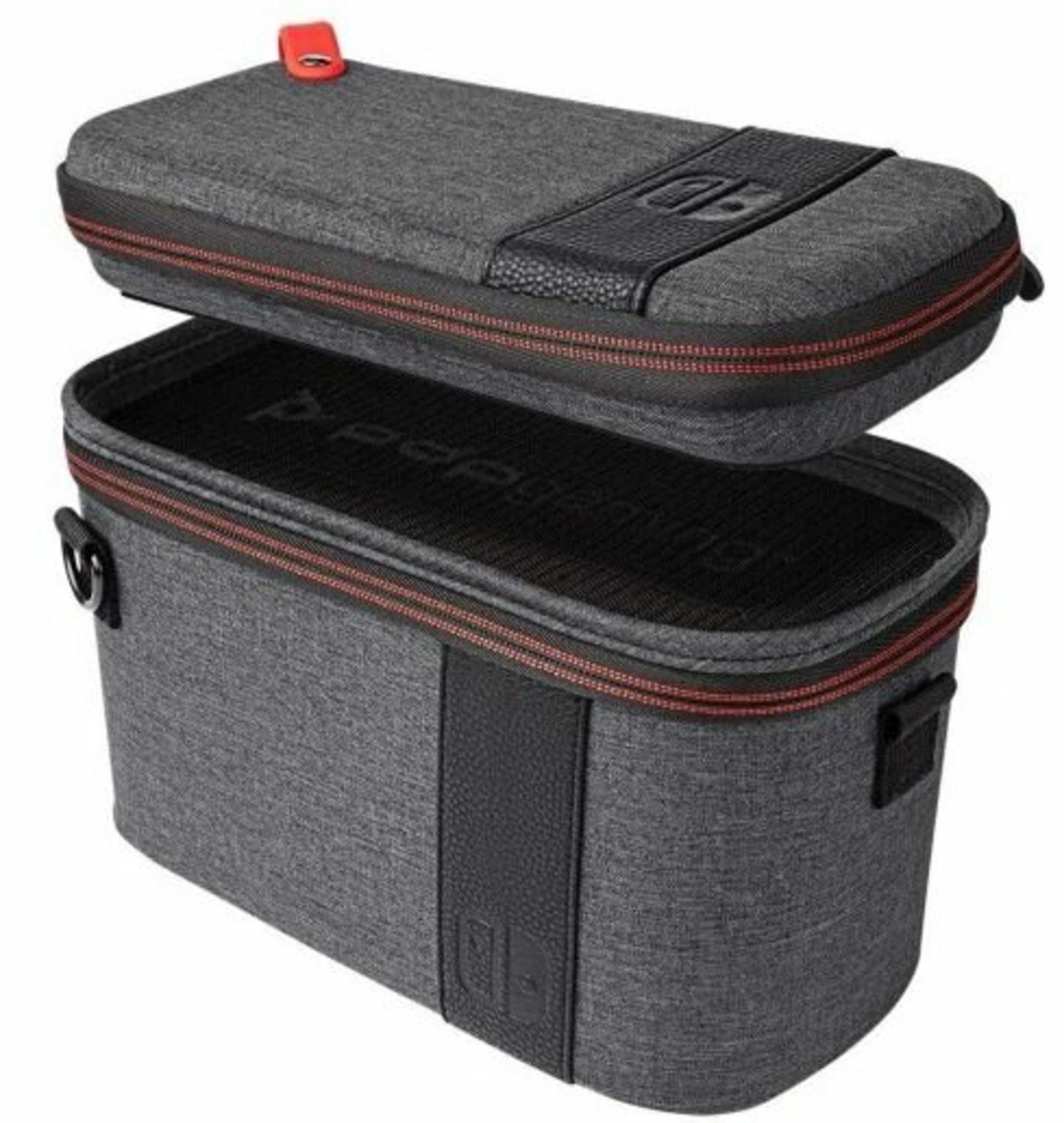 Ein grauer Koffer für eine Konsole ist geöffnet. Er hat einen roten Reißverschluss und einen schwarzen Griff. Der obere Teil ist offen.