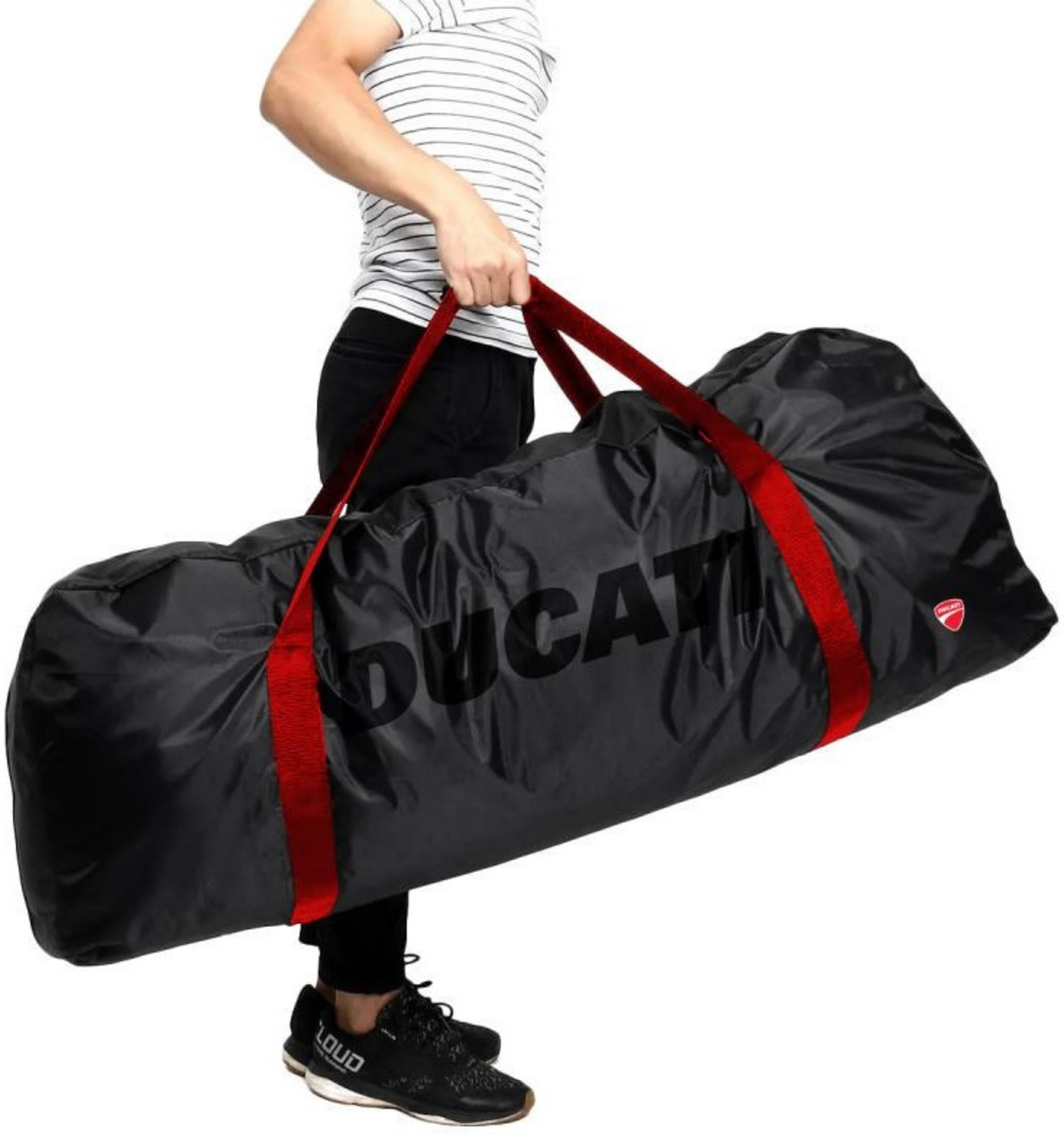 A person holds a black Ducati bag with red straps. The person wears a striped shirt and black pants.