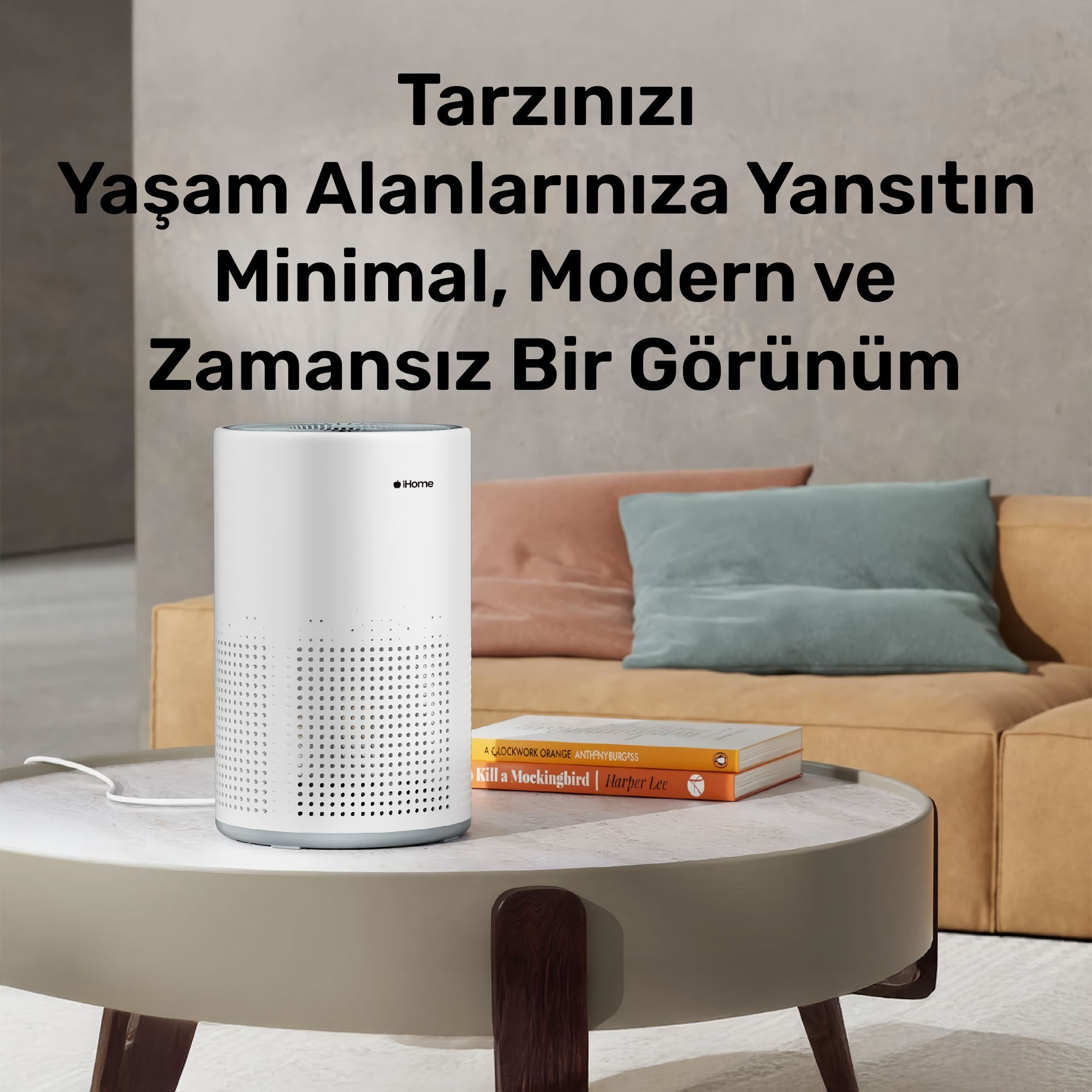 Kitaplarla dolu bir masanın üzerinde beyaz bir hava temizleyici. Arka planda bir kanepe ve yastıklar. Sahne modern.