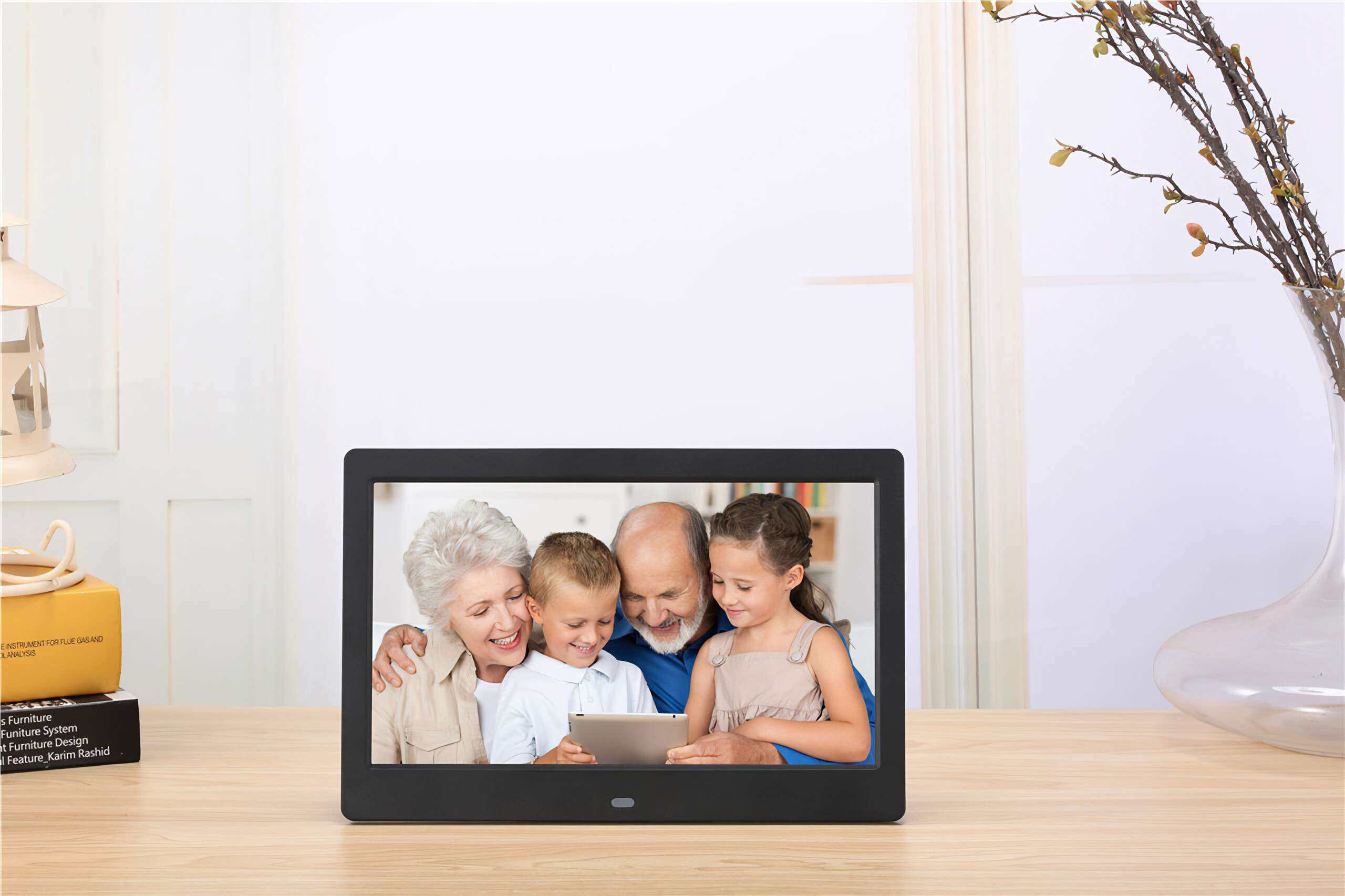 Ein digitaler Bilderrahmen zeigt eine Familie: Großeltern und Enkelkinder, die auf ein Tablet schauen. Der Rahmen steht auf einem Holztisch.