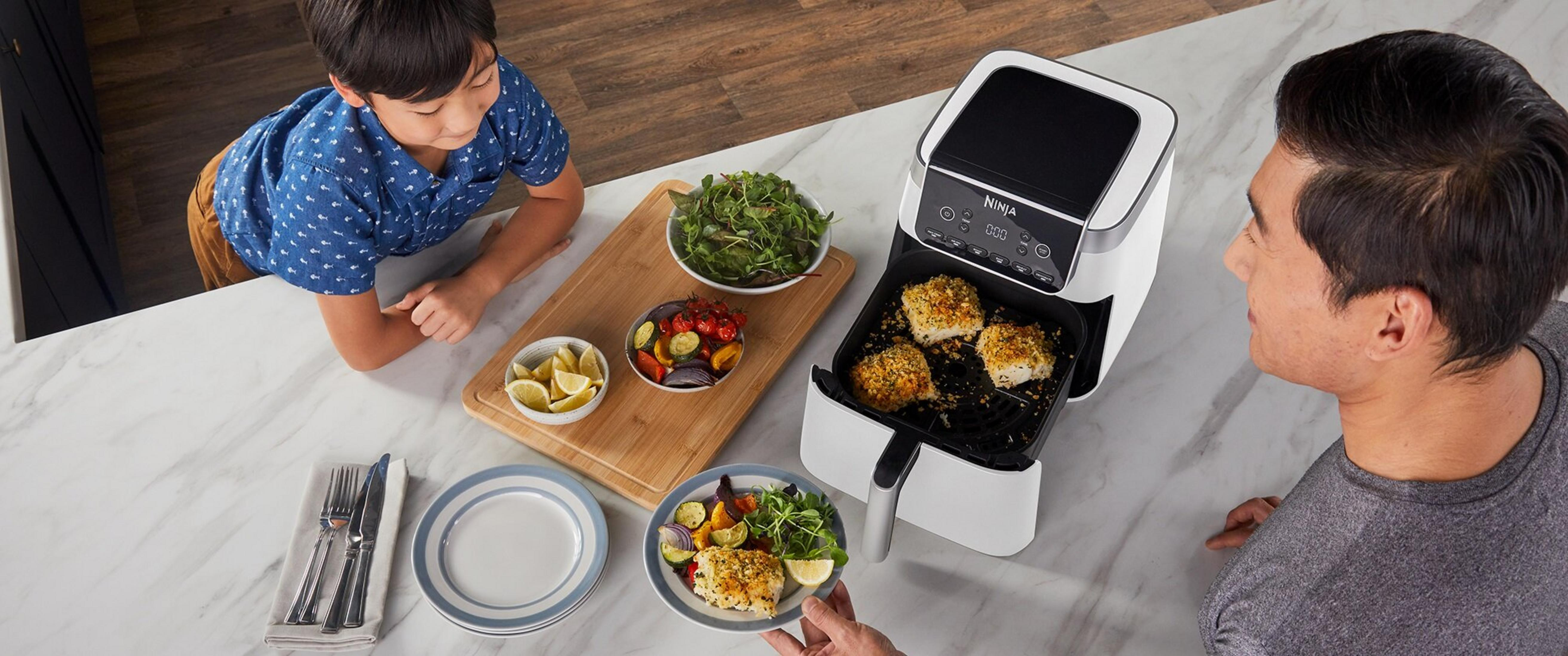 Rodzina przygotowuje posiłek z rybą i warzywami smażonymi na powietrzu. Obecny jest chłopiec i mężczyzna.