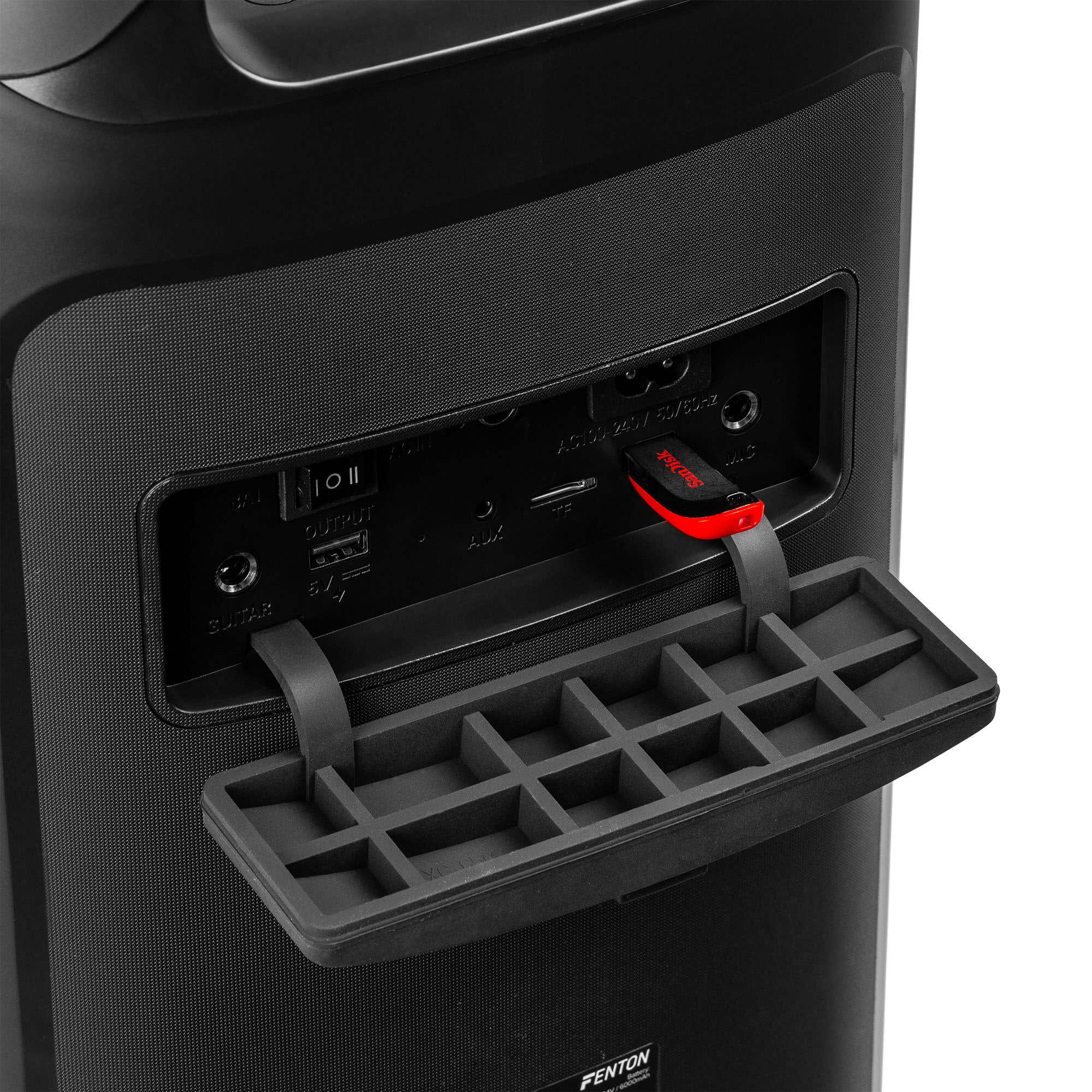 Primer plano de un altavoz negro con una unidad USB roja y negra insertada. Una bandeja está extendida.