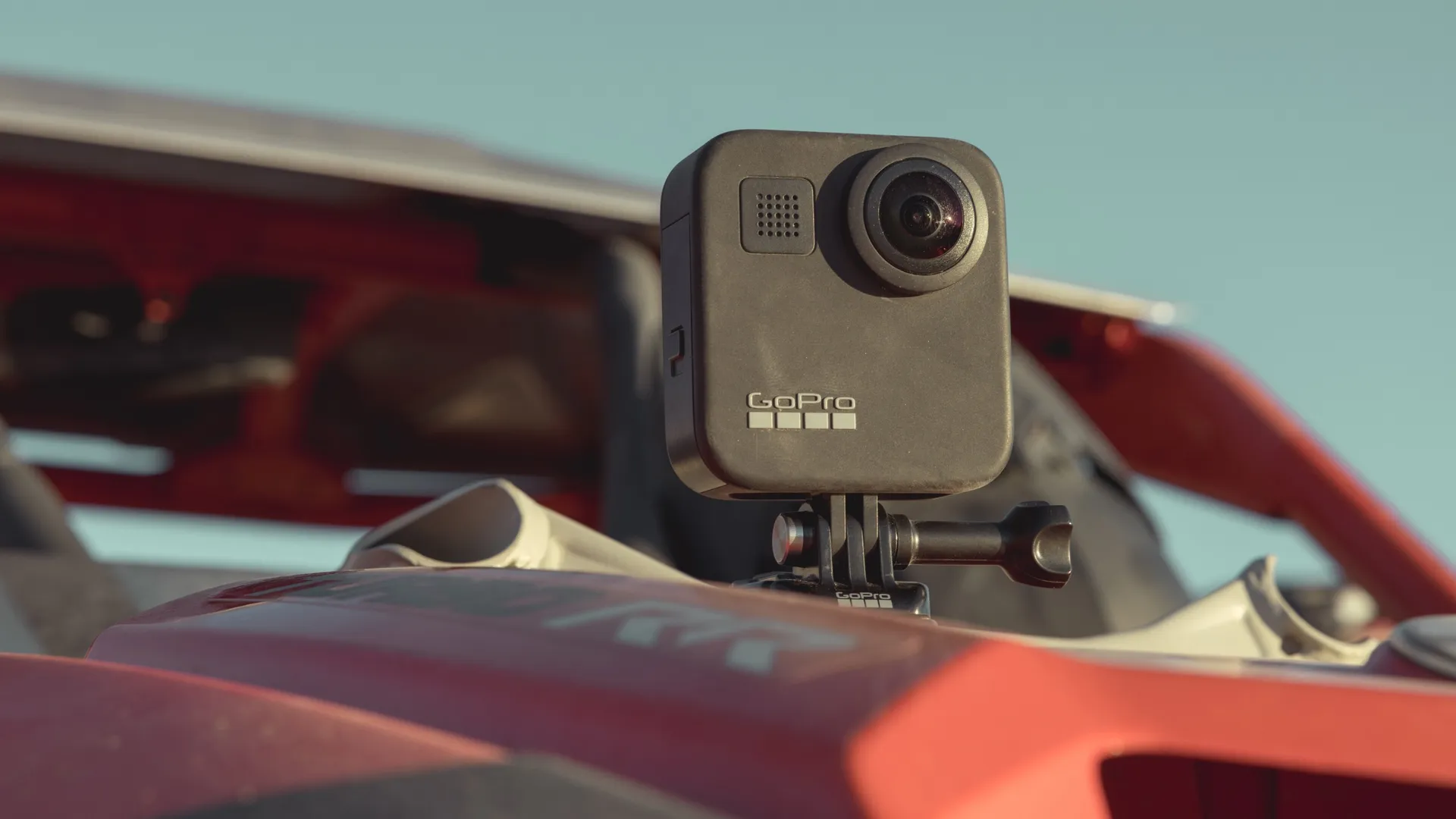 Kamera GoPro jest zamontowana na czerwonym pojeździe. Kamera jest czarna z obiektywem i logo GoPro. Błękitne niebo w tle.
