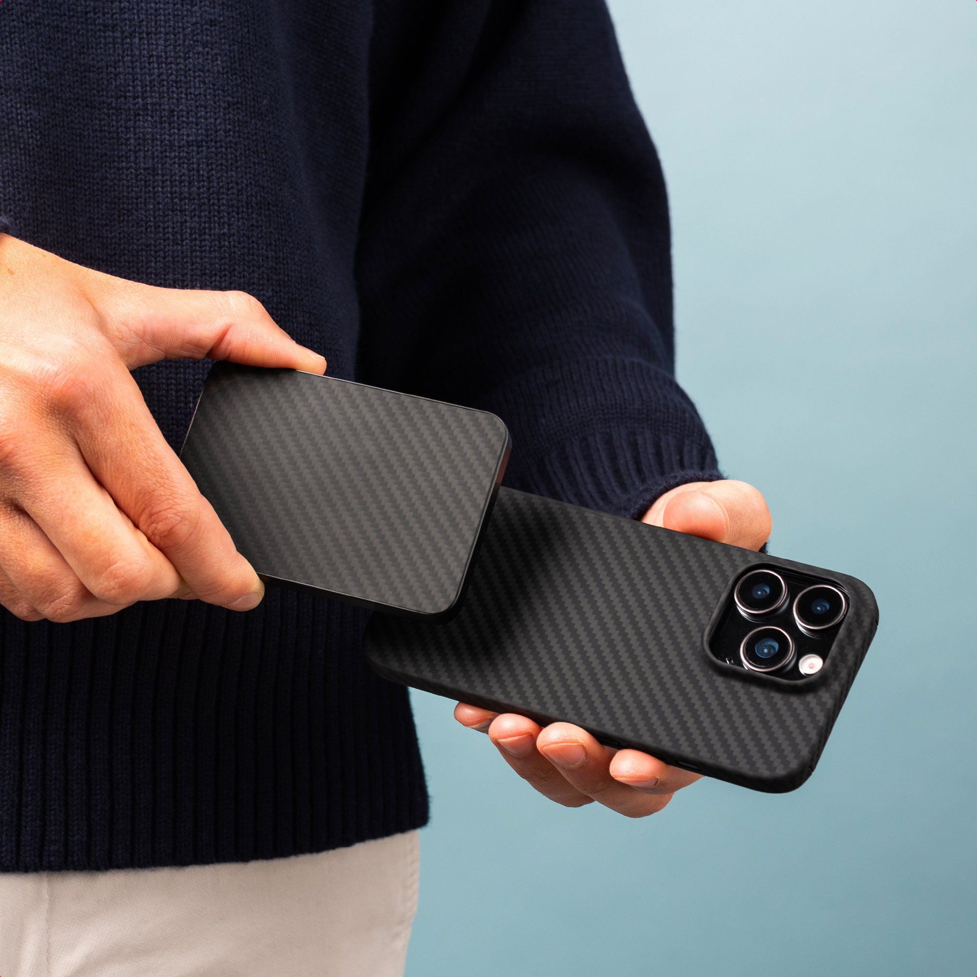 Une personne tient un étui de téléphone noir et un téléphone. Le fond est bleu clair.