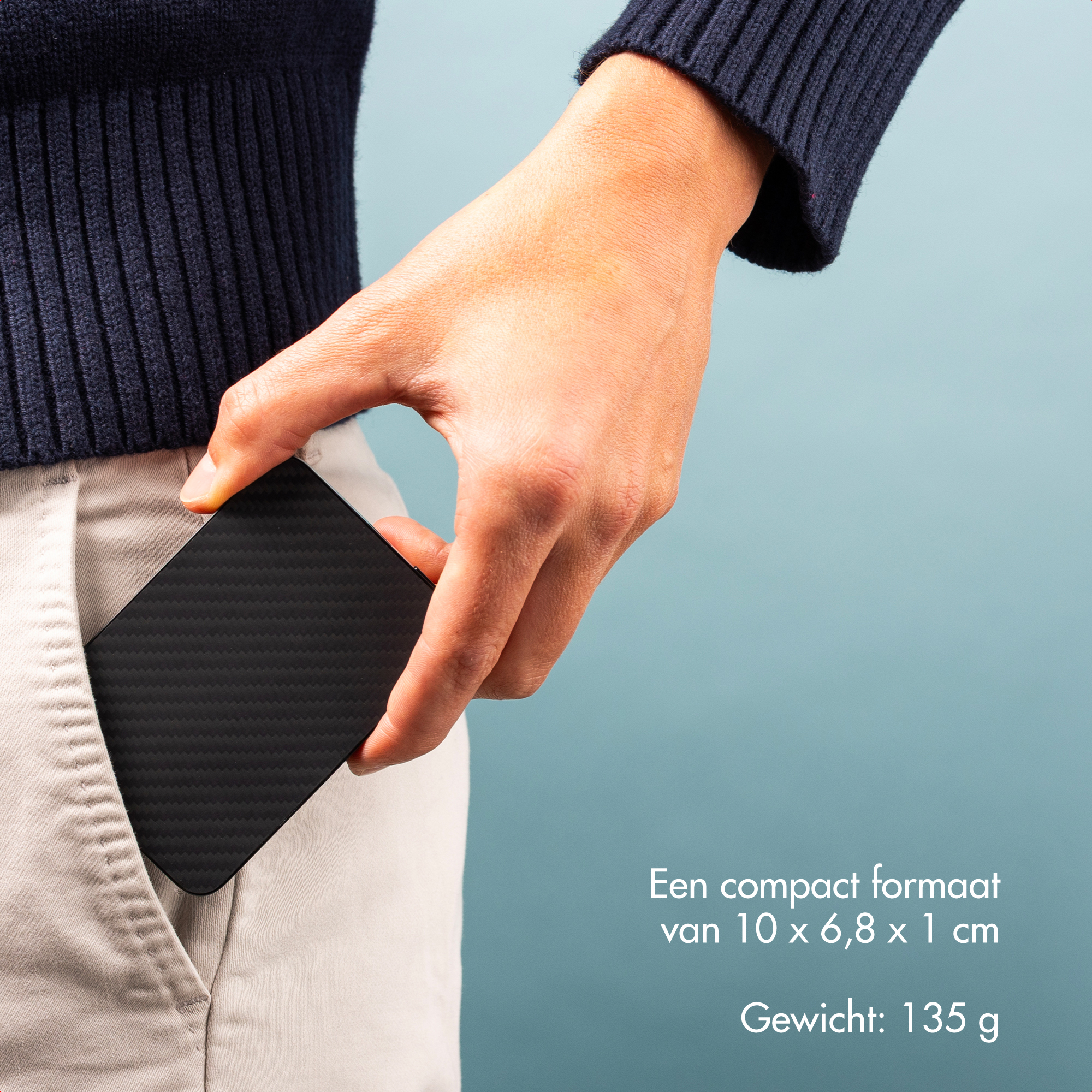 Une main met un objet noir en forme de carte dans une poche. La personne porte un pull marine et un pantalon beige.