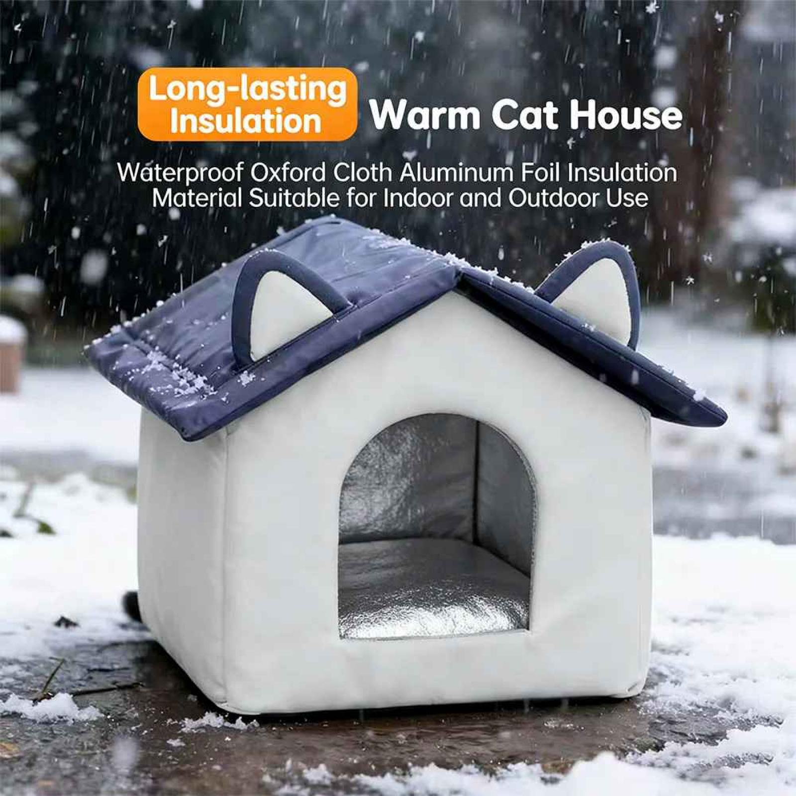 Ein weißes Katzenhaus mit dunkelblauem Dach und Ohren in einer verschneiten Umgebung im Freien. Es hat einen Bogeneingang.