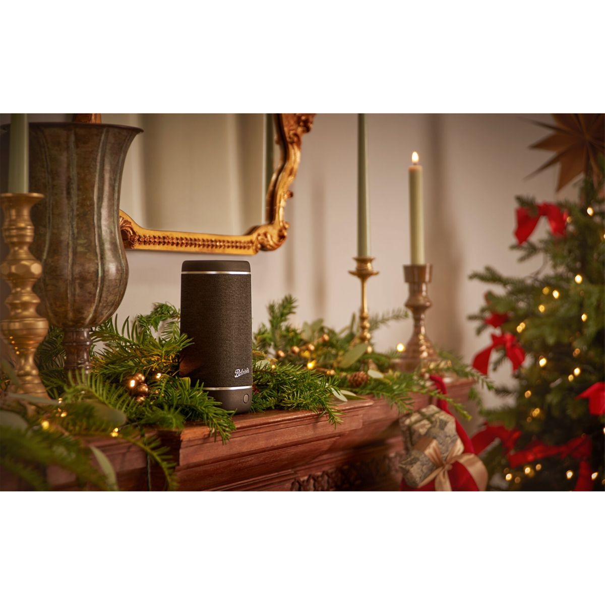 Ein Lautsprecher auf einem Kaminsims, der für Weihnachten dekoriert ist, mit Kerzen, Girlanden und einem Baum.