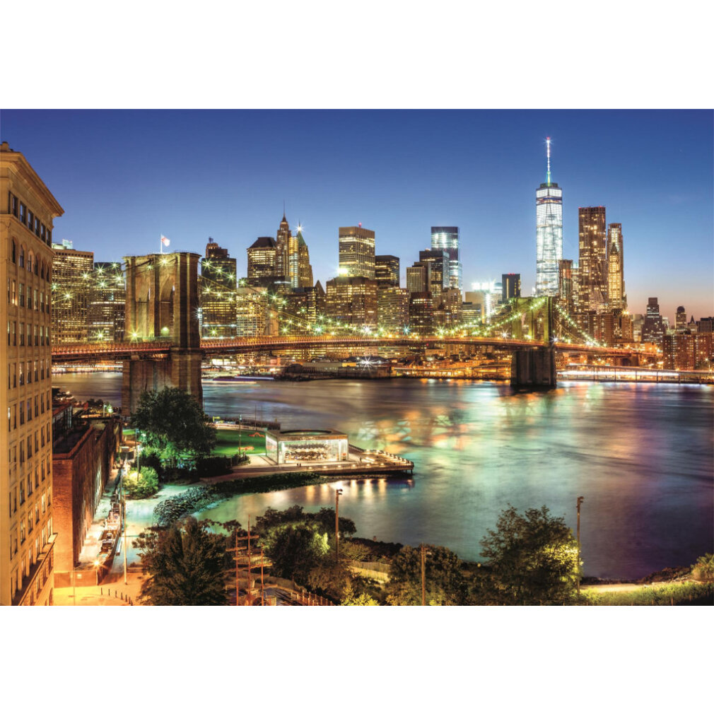 Brooklyn Bridge bei Dämmerung, Skyline im Hintergrund, Fluss im Vordergrund. Gebäude beleuchtet mit Lichtern, die sich im Wasser spiegeln.