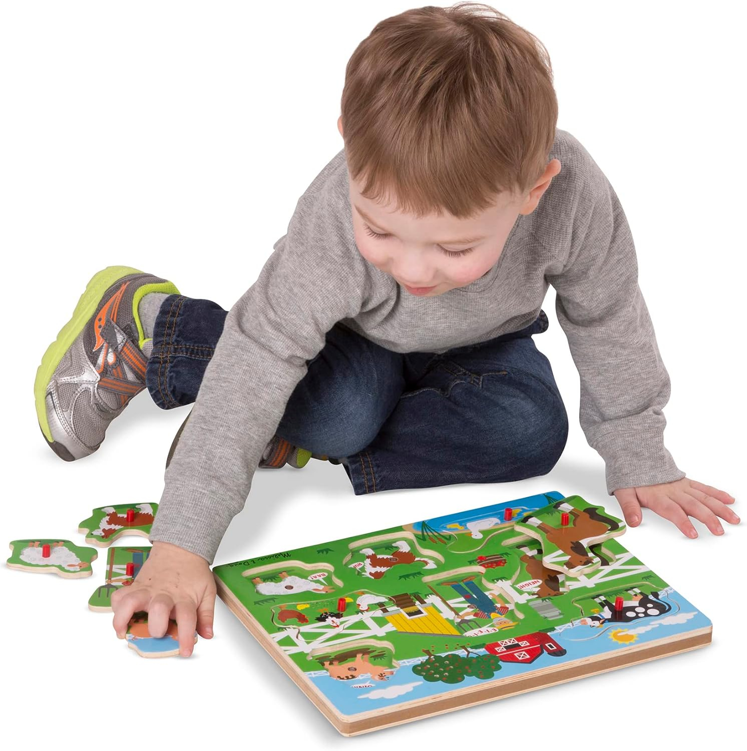 Ein Kind spielt mit einem Bauernhof-Puzzle. Das Puzzle liegt auf dem Boden, und das Kind legt ein Teil ein. Das Kind trägt ein graues Hemd.