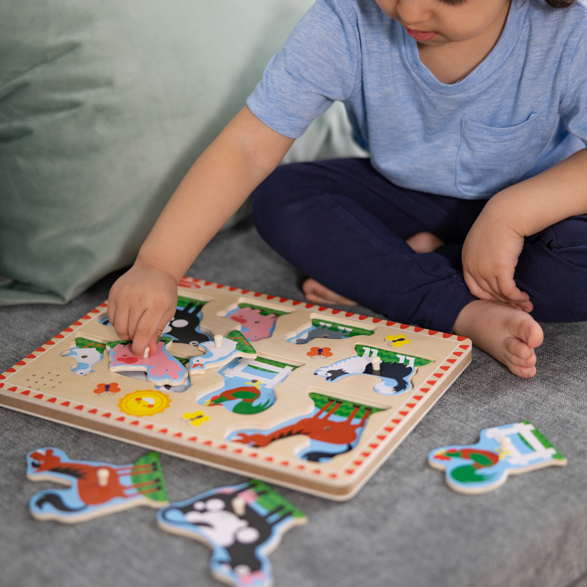 Ein Kind spielt mit einem Holzpuzzle. Das Puzzle hat Tierformen. Das Kind trägt ein blaues Hemd und sitzt auf einer Couch.