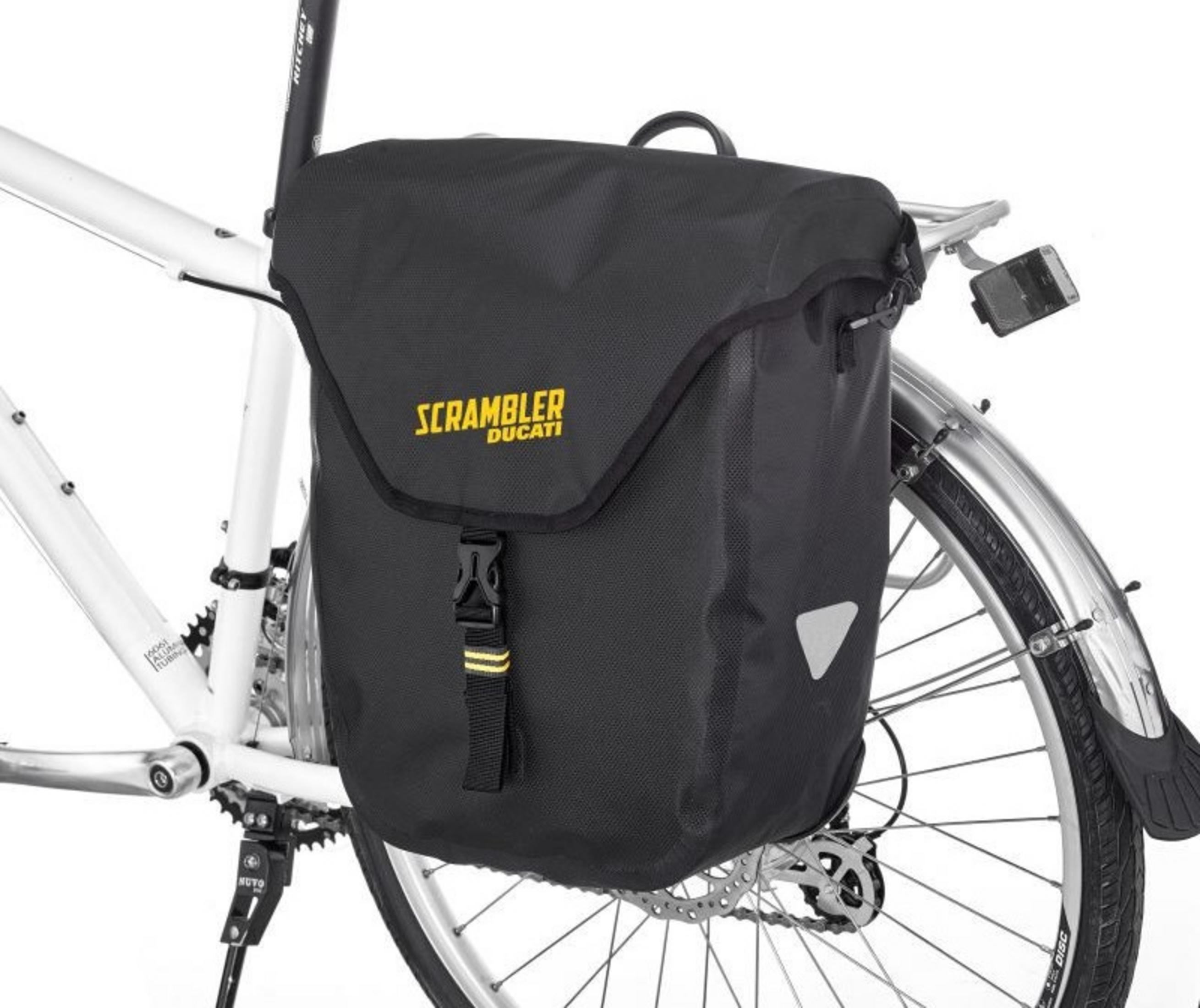 Schwarze Fahrradtasche mit gelbem 'Scrambler Ducati'-Logo, an einem weißen Fahrrad montiert. Reflektierende Elemente vorhanden.