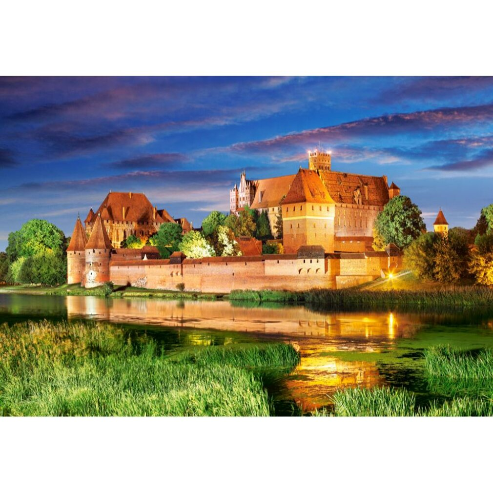 Eine große Burg mit roten Dächern und Türmen spiegelt sich im Wasser. Saftig grüne Vegetation umgibt die Burg und das Wasser.
