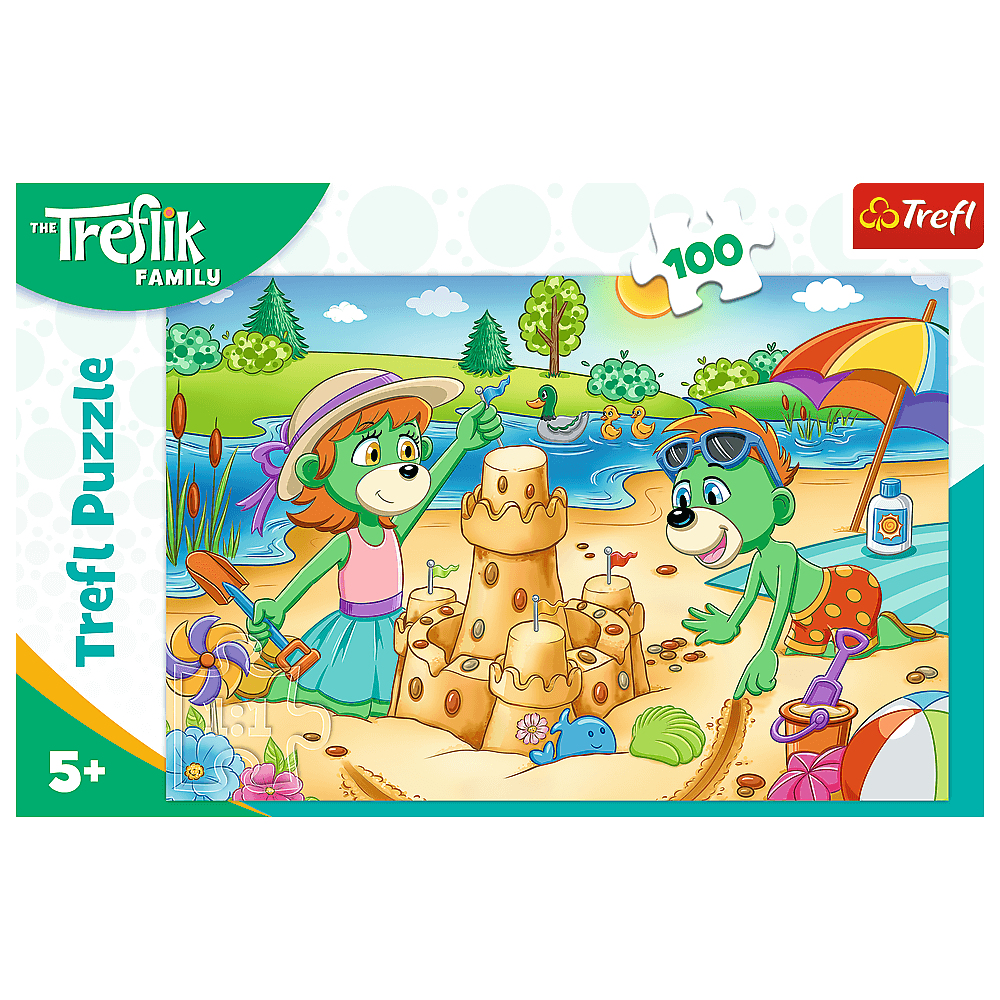 Ein Trefl-Puzzle zeigt grüne Cartoon-Figuren, die eine Sandburg am Strand bauen, mit Enten, einem Schirm und einem See im Hintergrund.