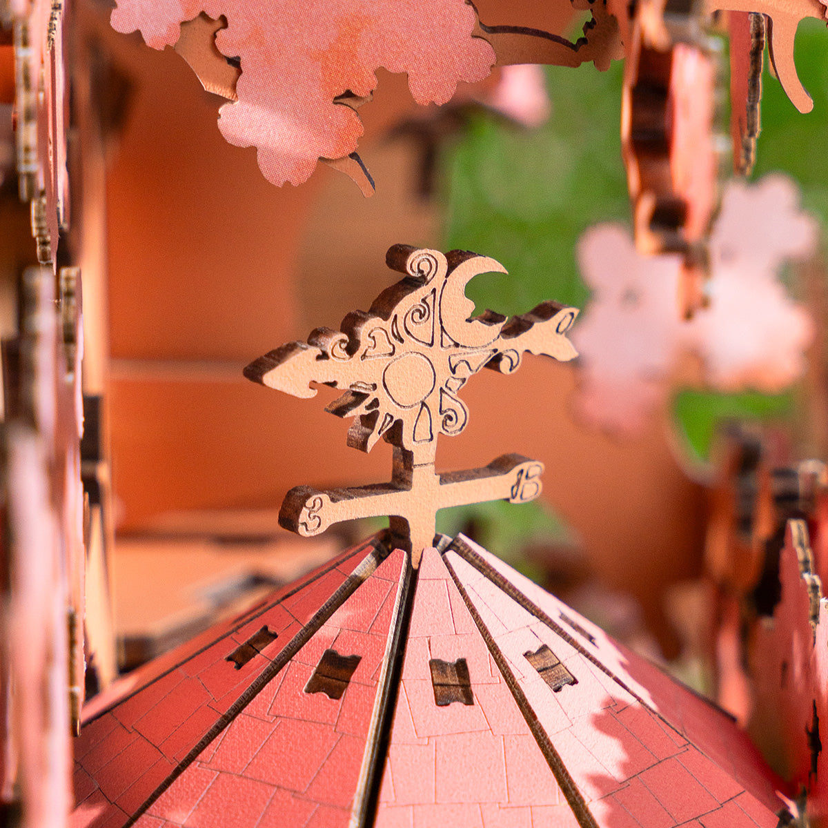 Nahaufnahme einer Holzkonstruktion. Ein rotes Dach trägt eine detaillierte Wetterfahne. Holzblumen-Ausschnitte umgeben die Szene.