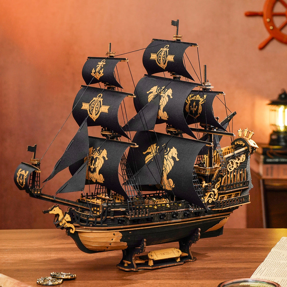 Un modèle de navire en bois détaillé. Voiles noires avec des emblèmes dorés, des accents dorés sur une coque noire, sur bois.