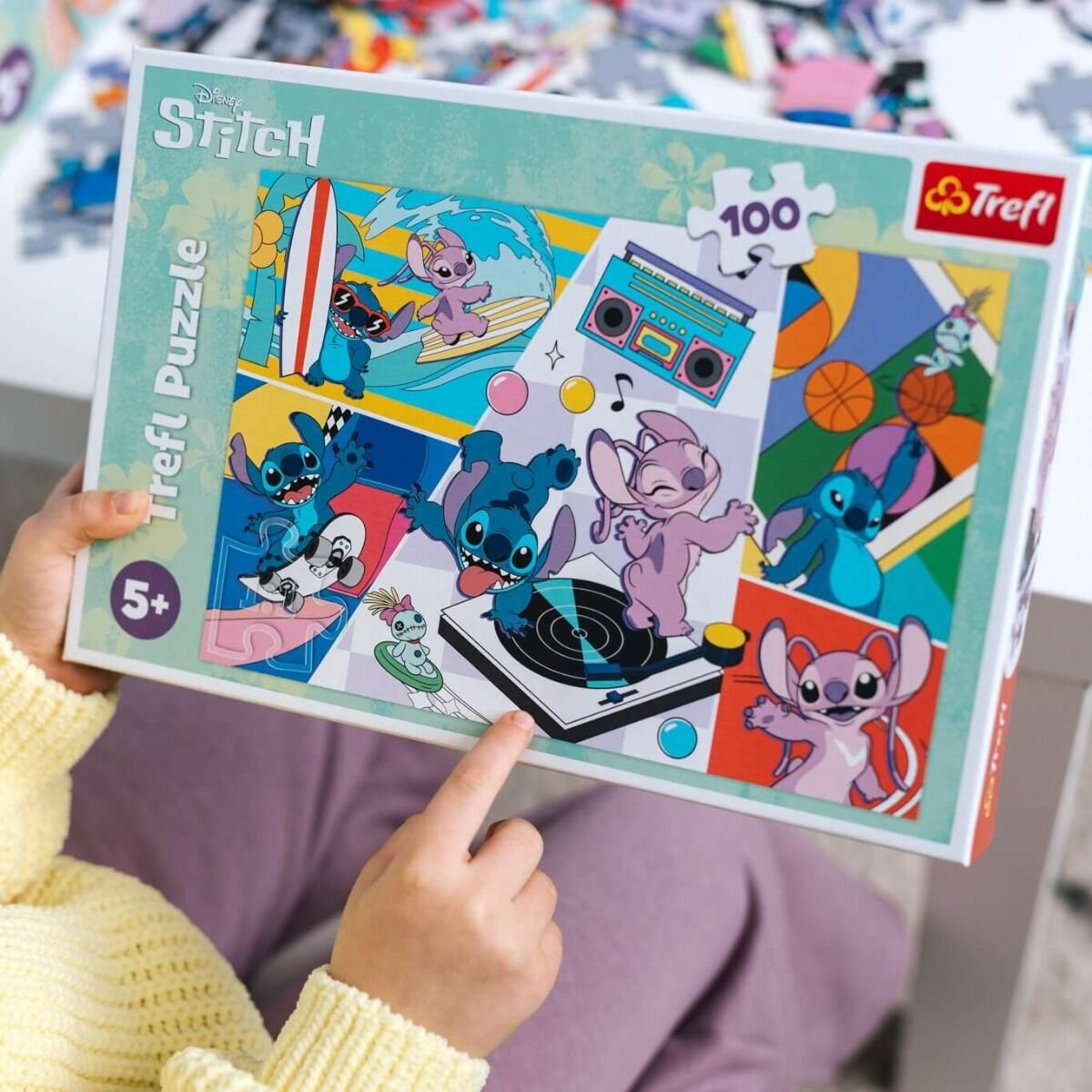 Kinderhände halten eine Stitch-Puzzlebox. Die Box zeigt Stitch-Charaktere beim Surfen, Skateboarden und Tanzen mit einer Boombox.