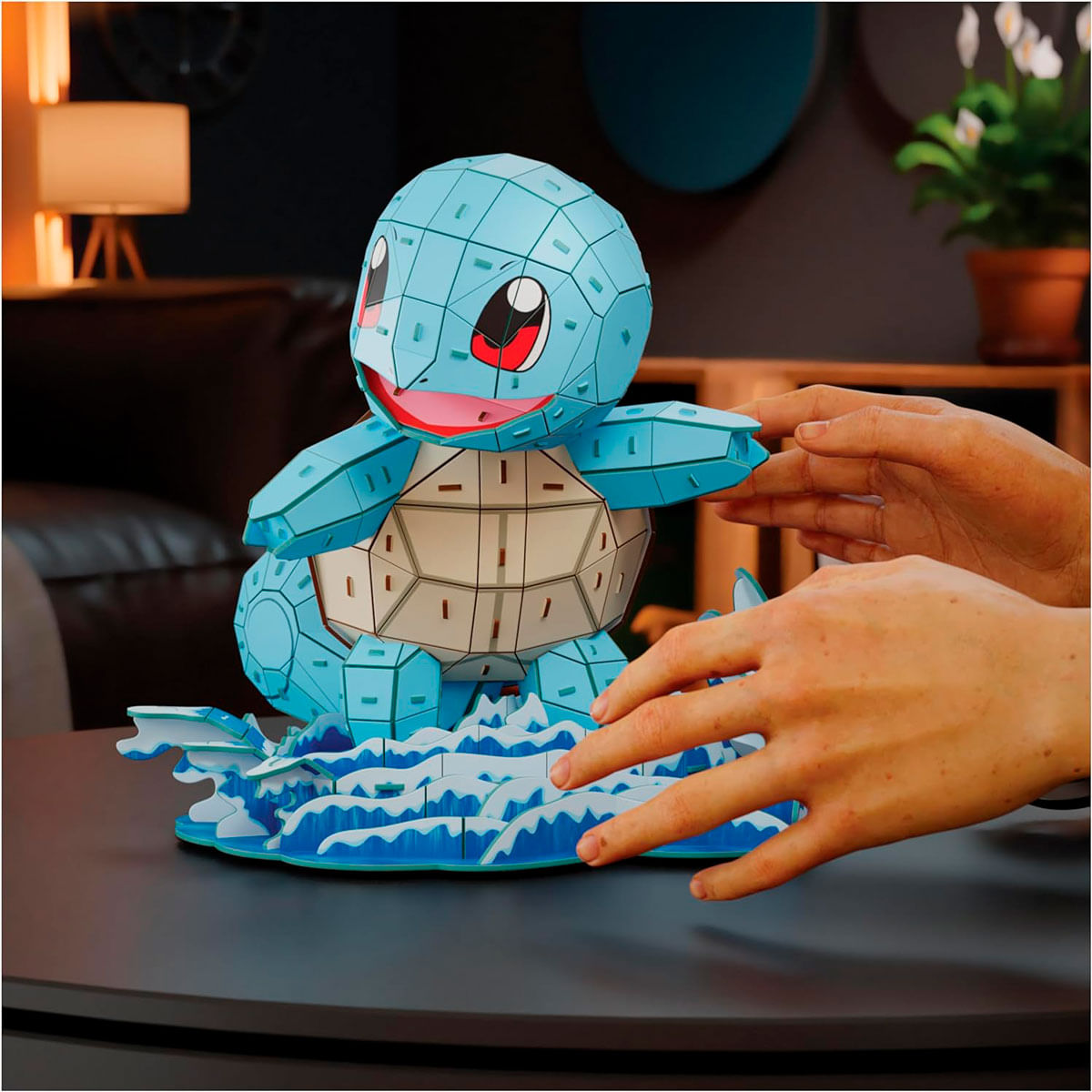 Ein blaues Squirtle-Puzzle ist zusammengesetzt. Hände interagieren mit dem Spielzeug. Der Hintergrund hat eine Lampe und einen Blumentopf.