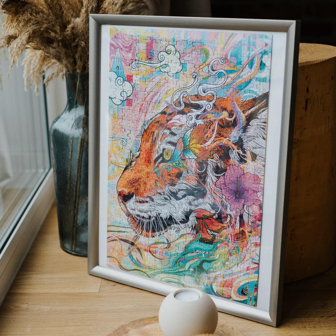 Ein gerahmtes Puzzle eines bunten Tigerkopfes. Eine Vase mit getrockneten Pflanzen und ein Kerzenhalter sind im Vordergrund.