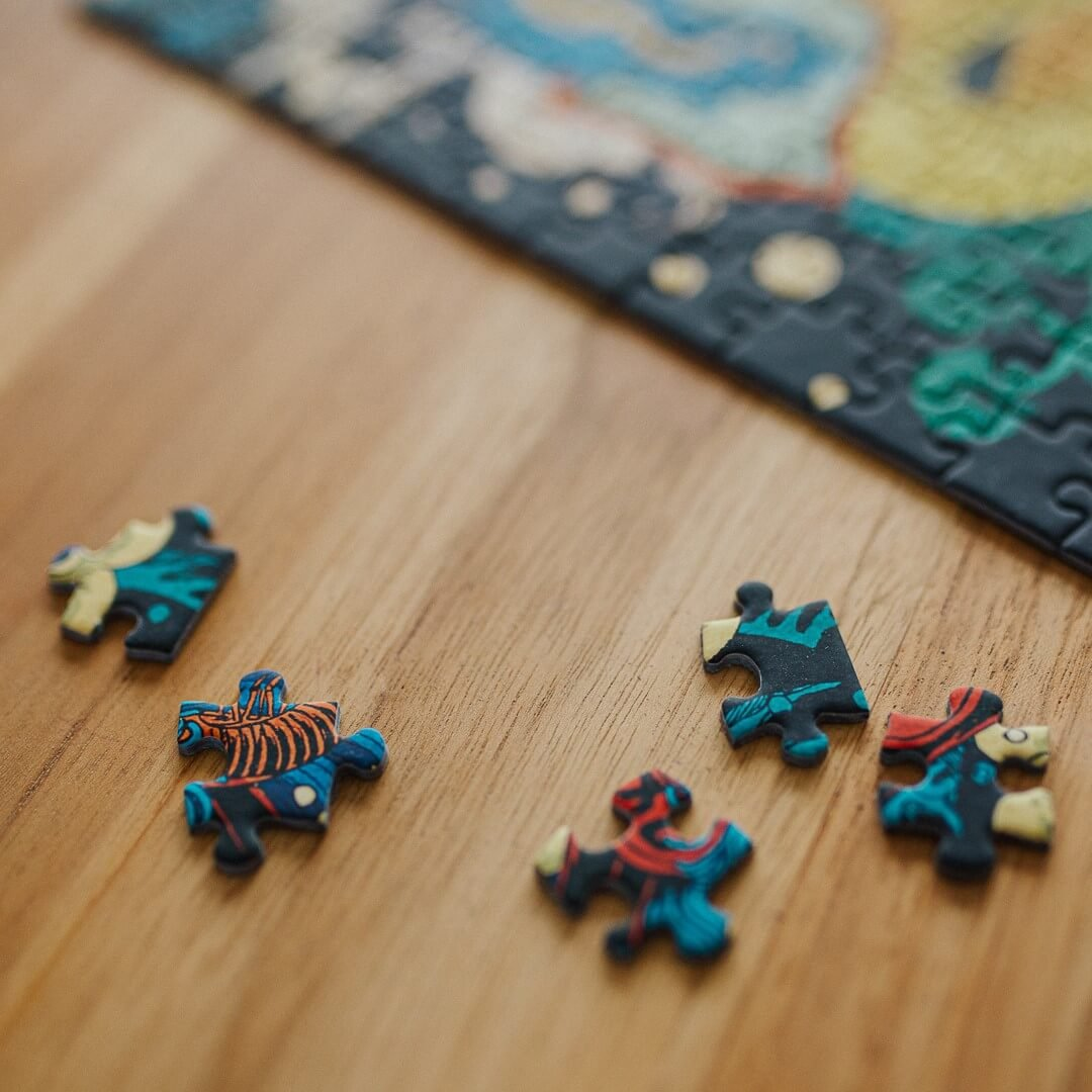 Holztisch mit verstreuten Puzzleteilen. Jedes Teil hat bunte Designs. Im Hintergrund befindet sich ein größeres Puzzle.