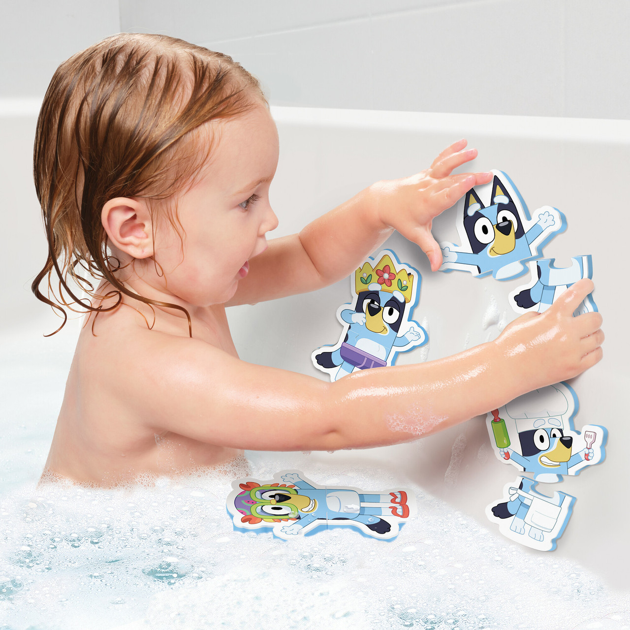 Ein Kind in einer Badewanne spielt mit Badespielzeug zum Thema Bluey. Die Spielzeuge sind farbenfroh und das Kind ist von Blasen umgeben.
