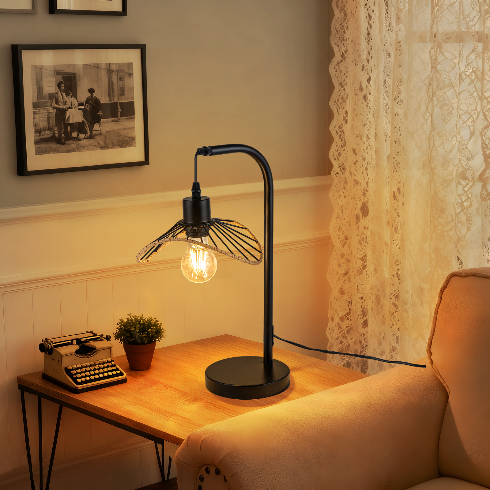 Una lámpara de escritorio con una bombilla vintage está sobre una mesa de madera. También hay una máquina de escribir, una planta en maceta y una foto.