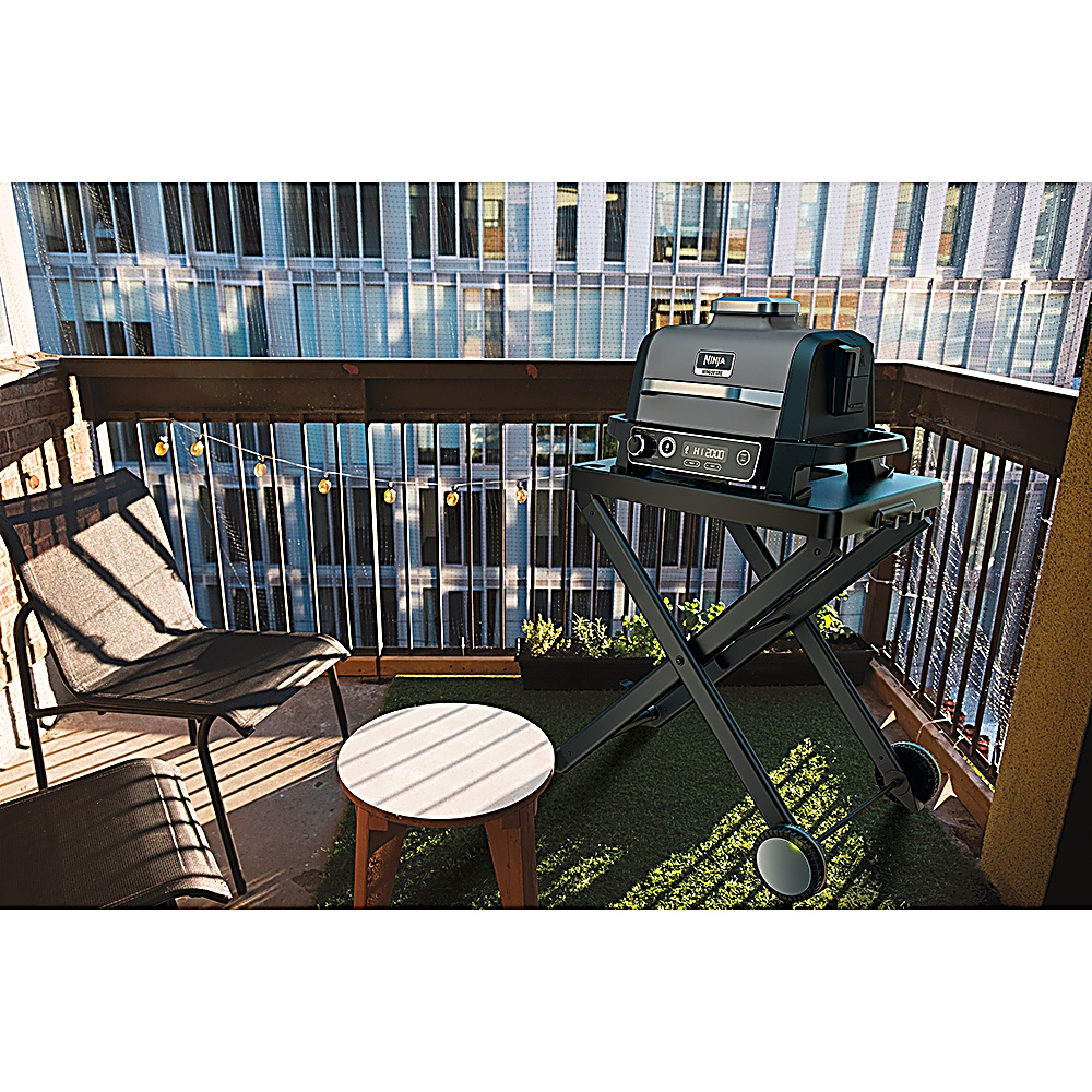 Czarny grill na balkonie z krzesłem i małym stolikiem. W tle budynek miejski.