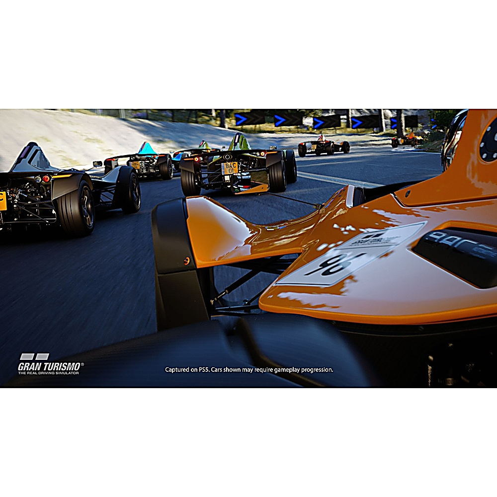 Coches de carreras a gran velocidad en una pista. El coche líder es naranja, otros son negros y verdes. El fondo tiene árboles y señales.