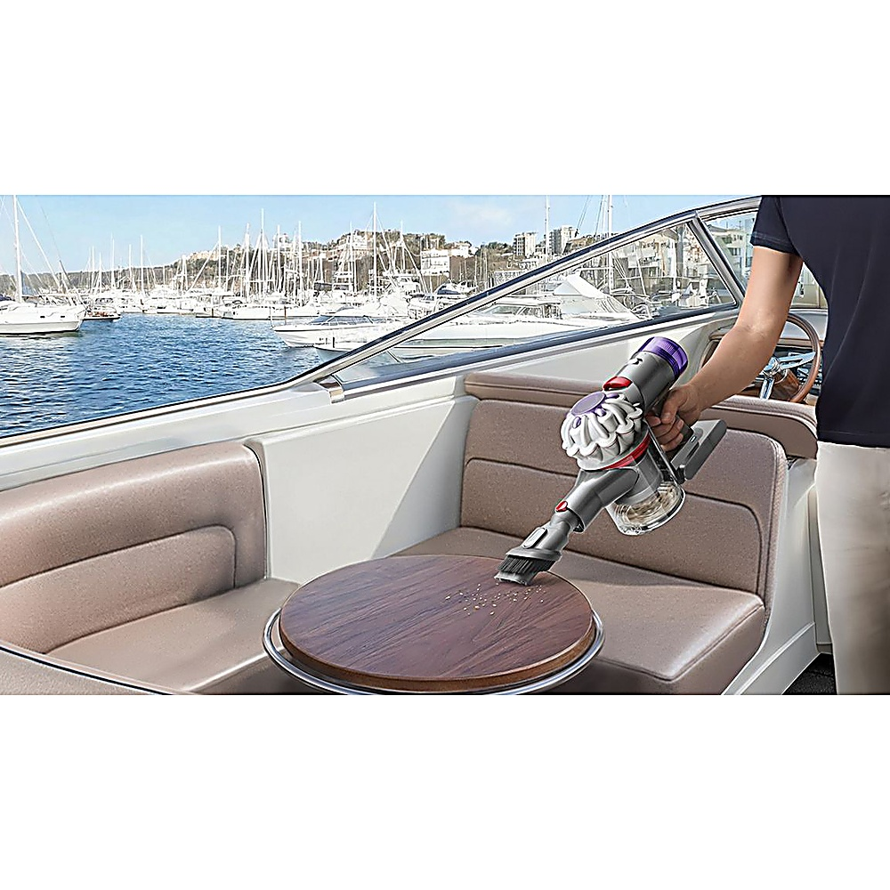 Eine Person saugt das Innere eines Bootes mit einem Handstaubsauger. Das Boot ist angedockt, im Hintergrund sind mehrere andere Boote zu sehen.