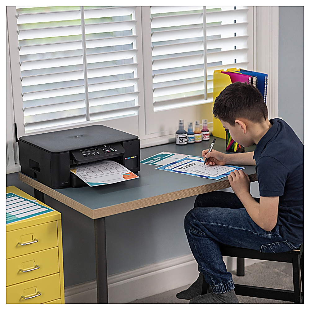 Chłopiec siedzi przy biurku, pisząc na arkuszu obok drukarki. Żółta szafka i okno w tle.