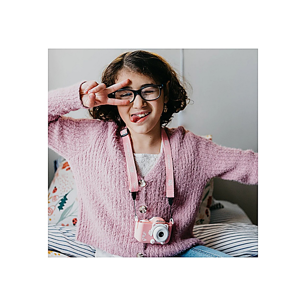 Una niña con gafas hace la señal de la paz, sacando la lengua. Lleva un suéter rosa, una cámara cuelga de su cuello.