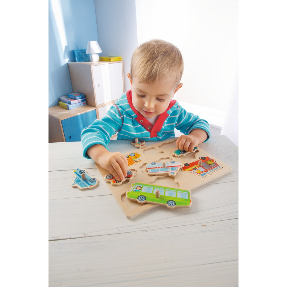 Un bambino gioca con un puzzle in legno di veicoli. Sta mettendo i pezzi sul puzzle. Il puzzle è su un tavolo bianco.