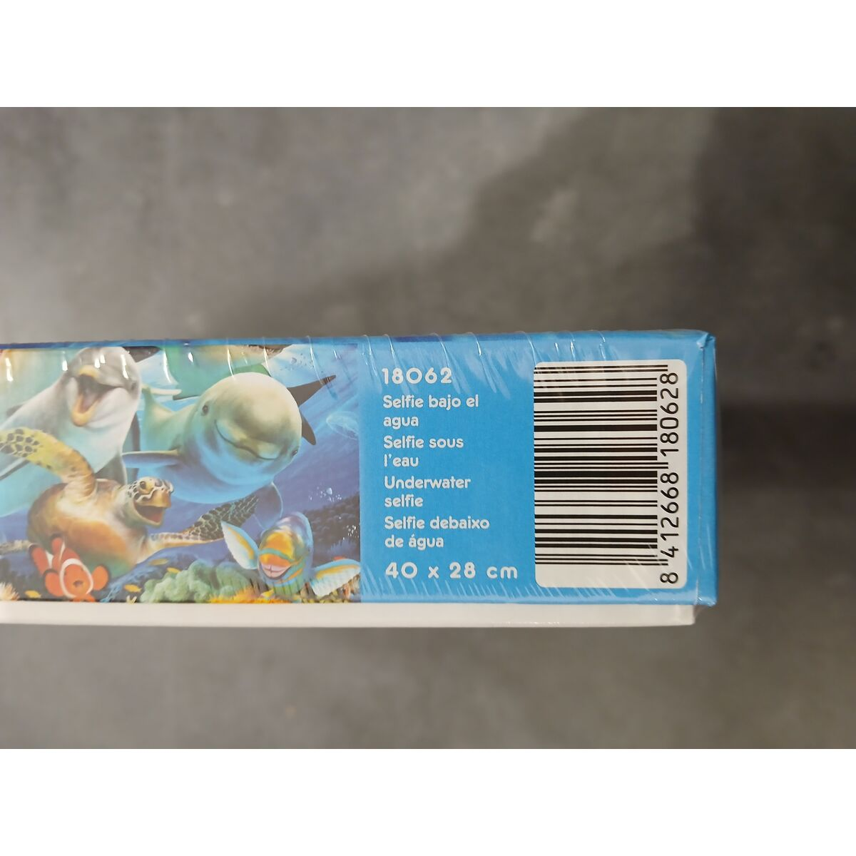 Die Seite einer Schachtel zeigt ein Puzzle mit Unterwassertieren. Ein Delfin, eine Schildkröte, Fische und Text in mehreren Sprachen sind zu sehen.