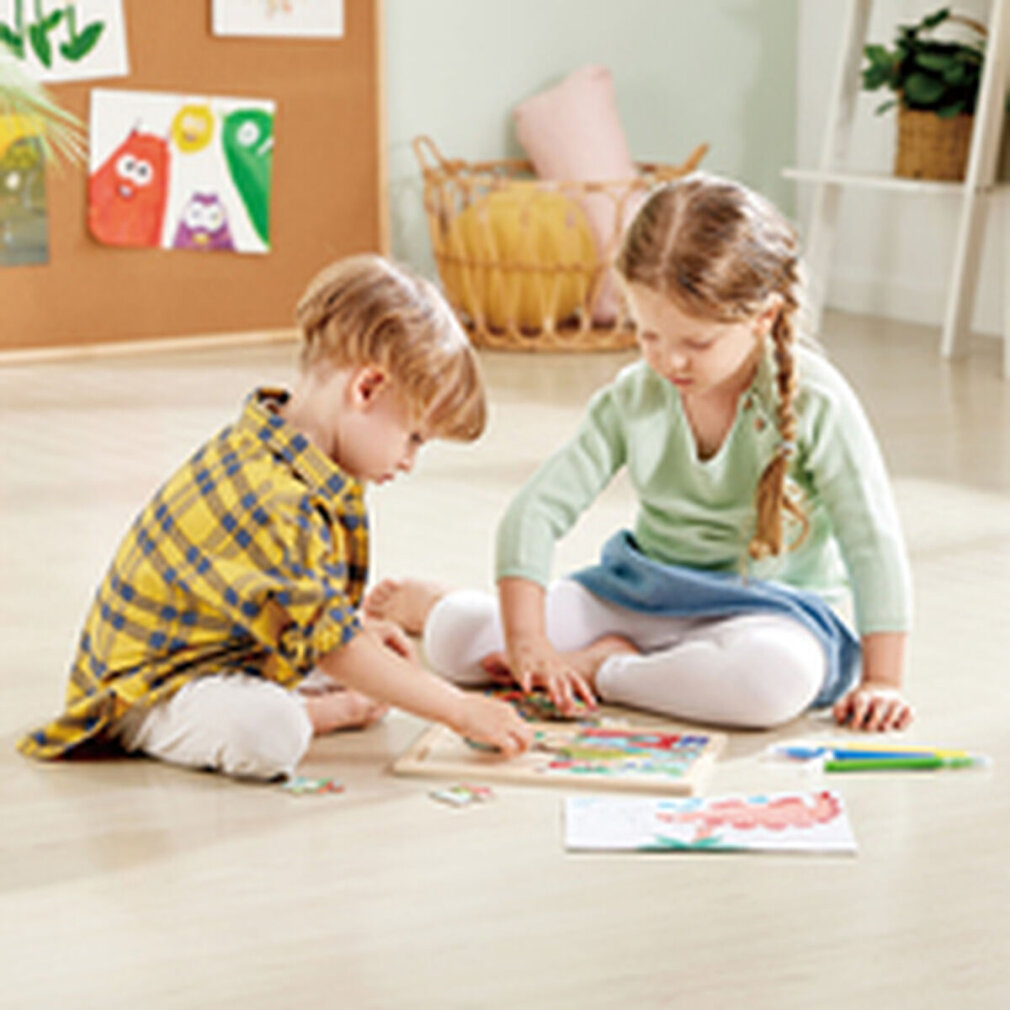 Zwei Kinder sitzen auf dem Boden und machen ein Puzzle. Einer trägt ein gelb kariertes Hemd. Die andere hat einen Zopf. Kunst an der Wand.