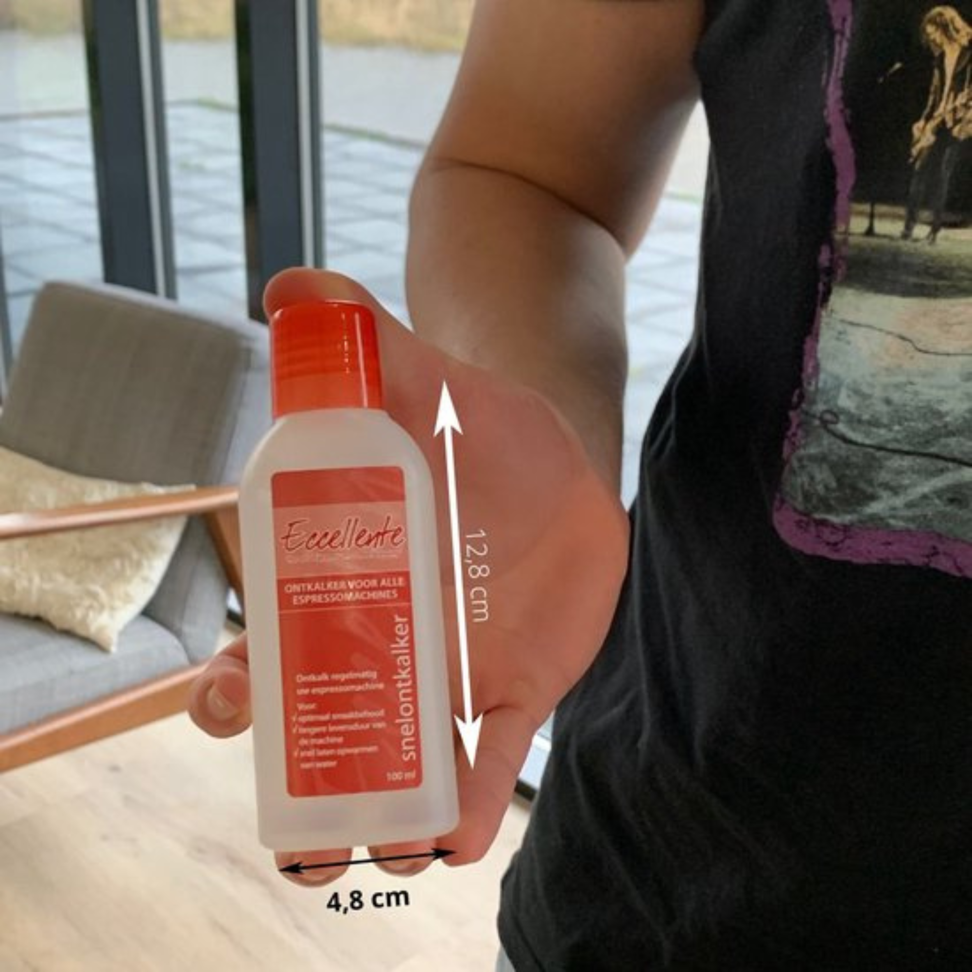 Une main tient une bouteille de détartrant pour machines à expresso. Blanche avec bouchon et étiquettes rouges, dimensions indiquées.