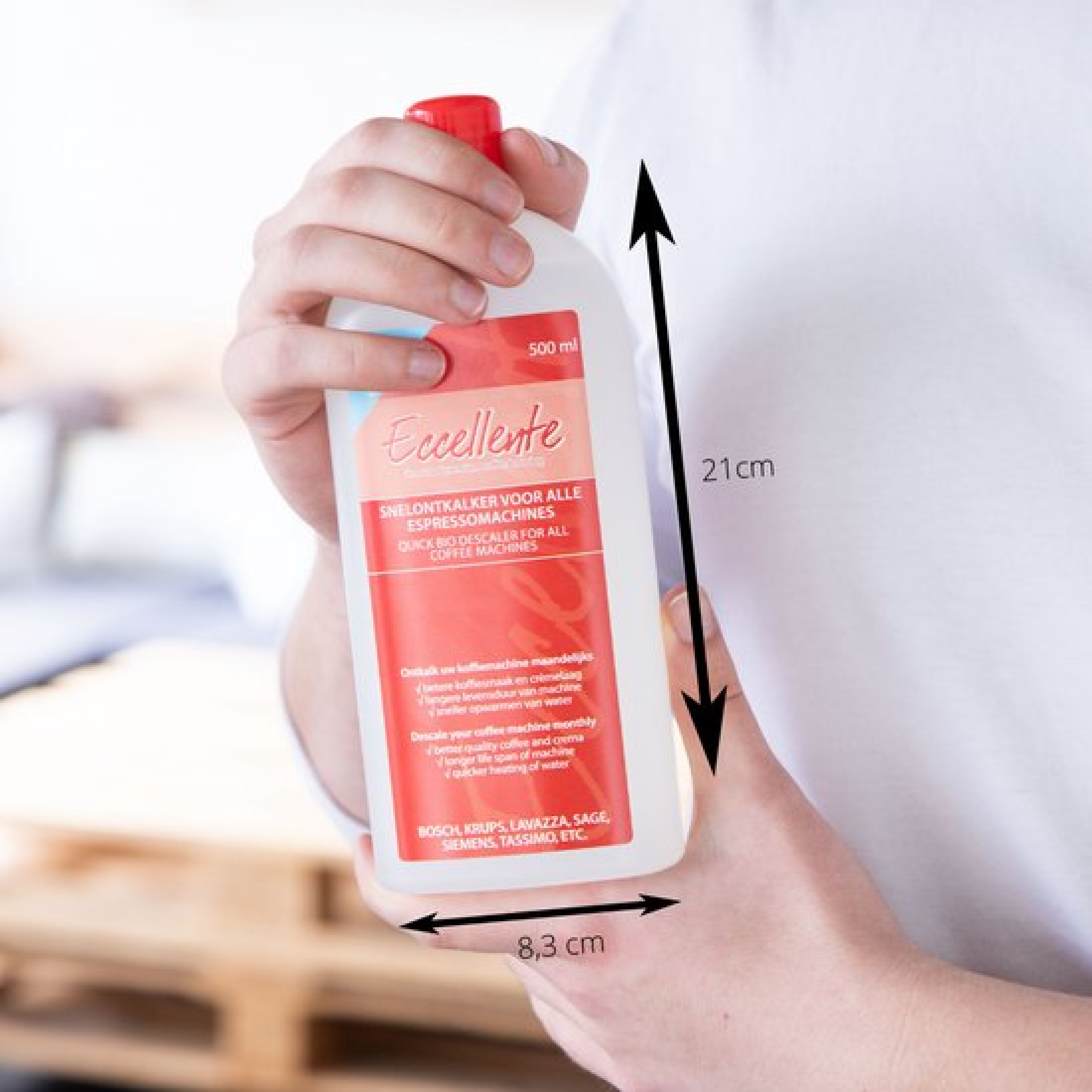 A person holds a bottle of descaler for coffee machines. The bottle is white with a red label. Dimensions are shown.